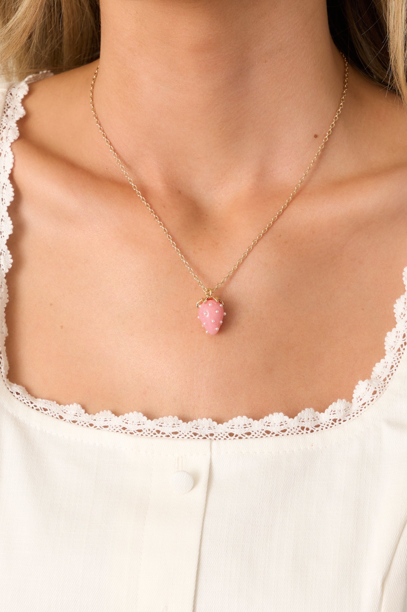 A gold chain necklace featuring a pink acrylic strawberry charm, accented with ivory faux pearl "seeds" for a playful and delicate touch.