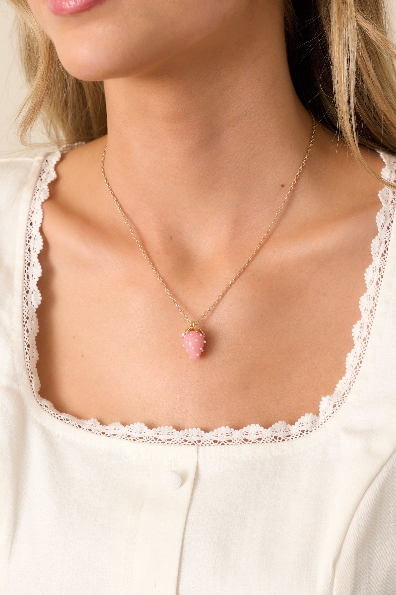 A detailed view of the pink strawberry charm, highlighting its glossy acrylic design, faux pearl accents, and gold chain for a whimsical look.