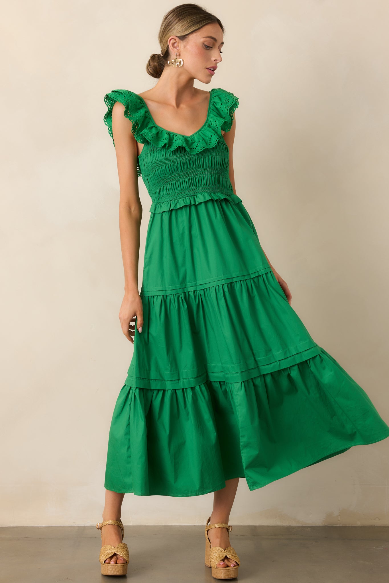  A green maxi dress with a ruffled V-neckline, smocked bodice, and a tiered skirt, flowing effortlessly. Functional pockets add a practical touch.