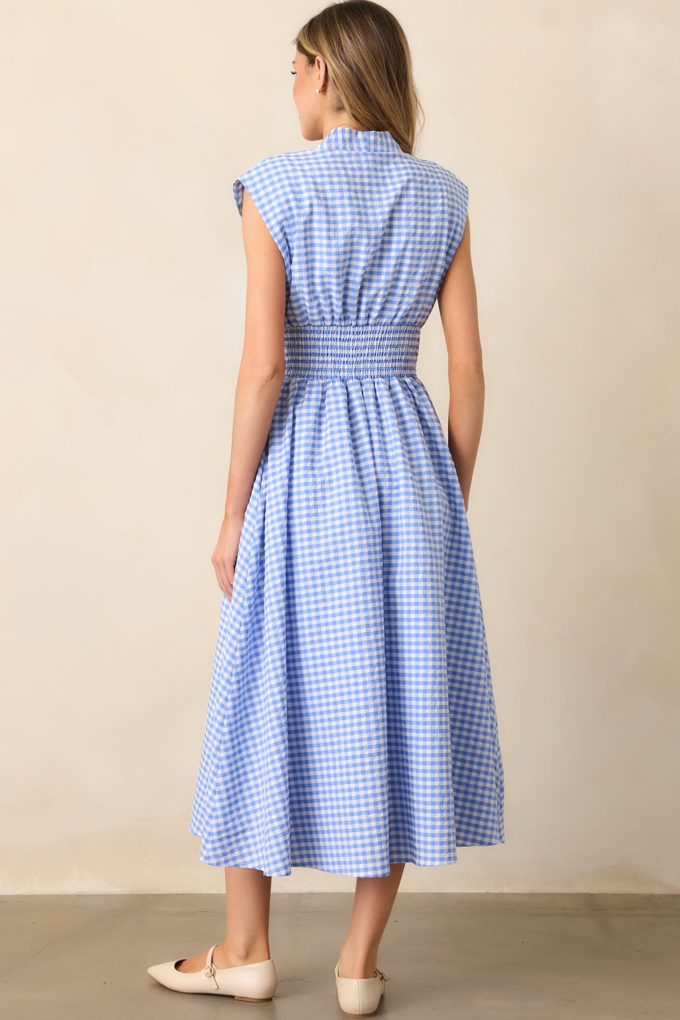 A view of the blue gingham midi dress from behind, showcasing the padded shoulders, smocked waist, and the overall fit.