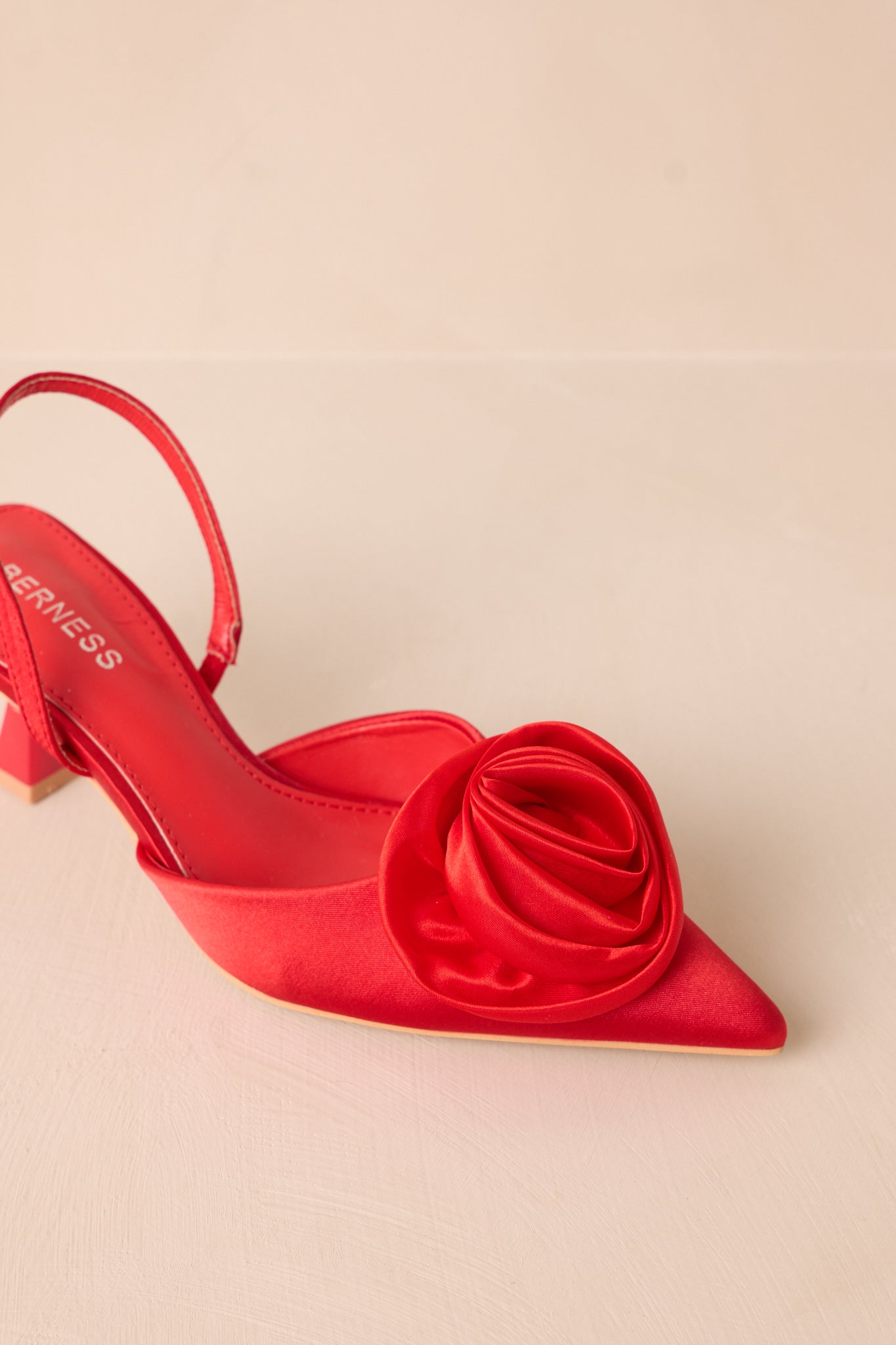 An angled close-up showing the red pointed toe and vibrant rose accent.