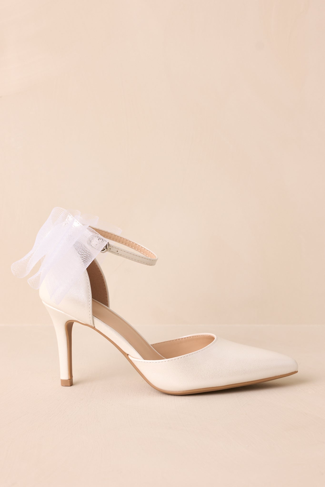 A side view of the ivory heels, showcasing the thin ivory heel and the large layered ivory lace bow at the back of the ankle.