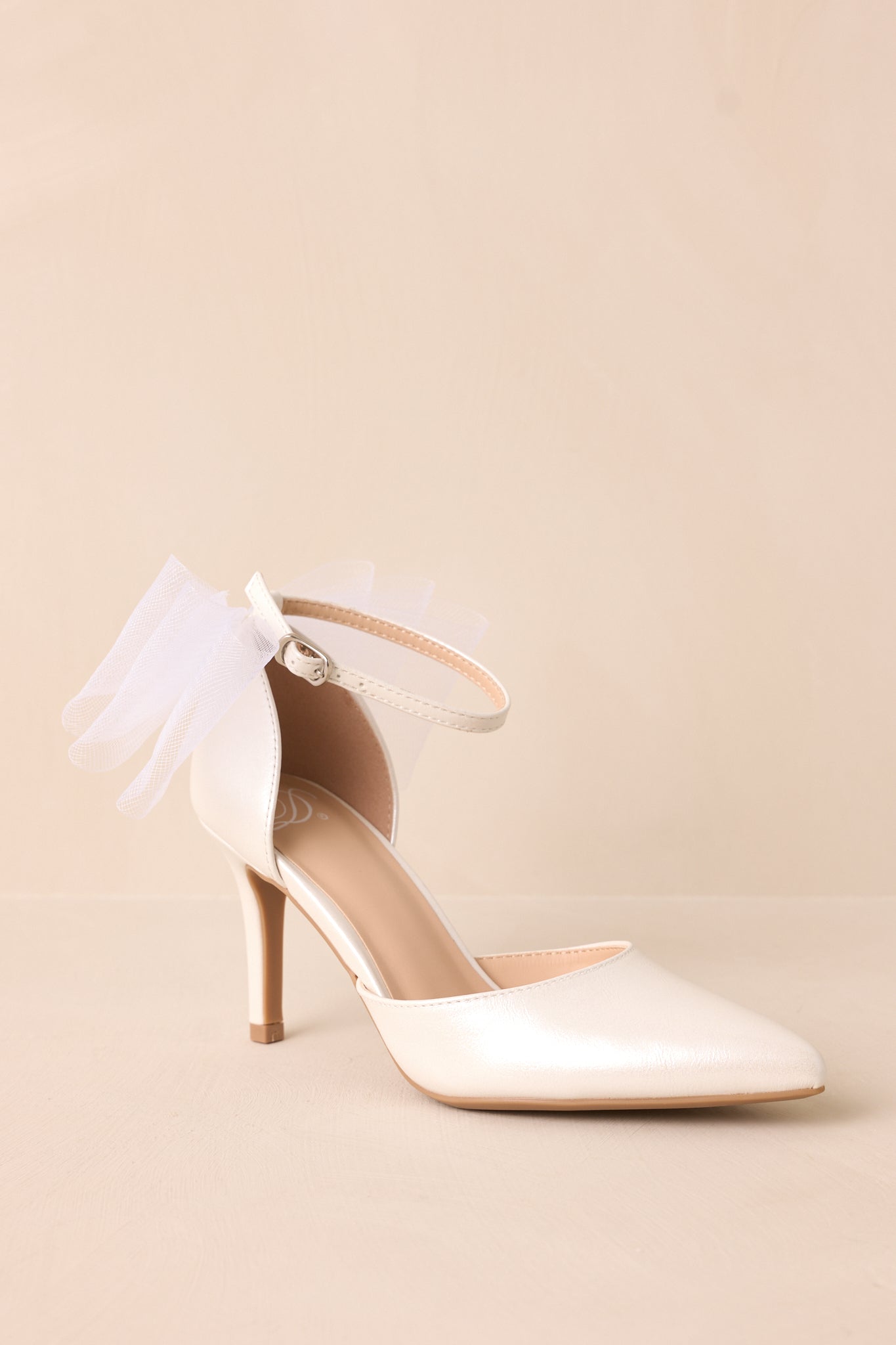 A three-quarter angle of the ivory heels, showcasing the delicate balance between the pointed toe, thin heel, and intricate lace bow detail.