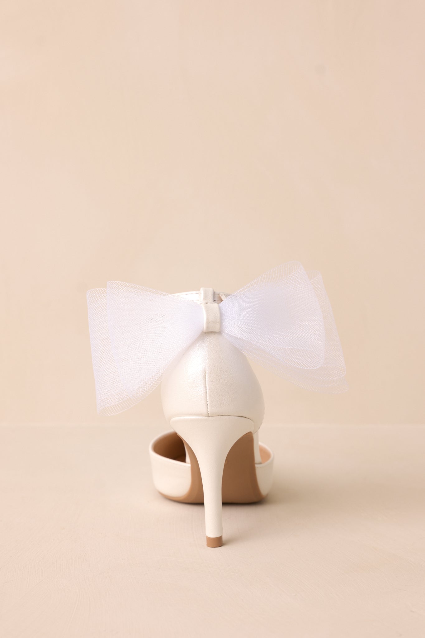  A back view of the ivory heels, focusing on the lace bow detail and thin ivory heel for a graceful, statement-making finish.