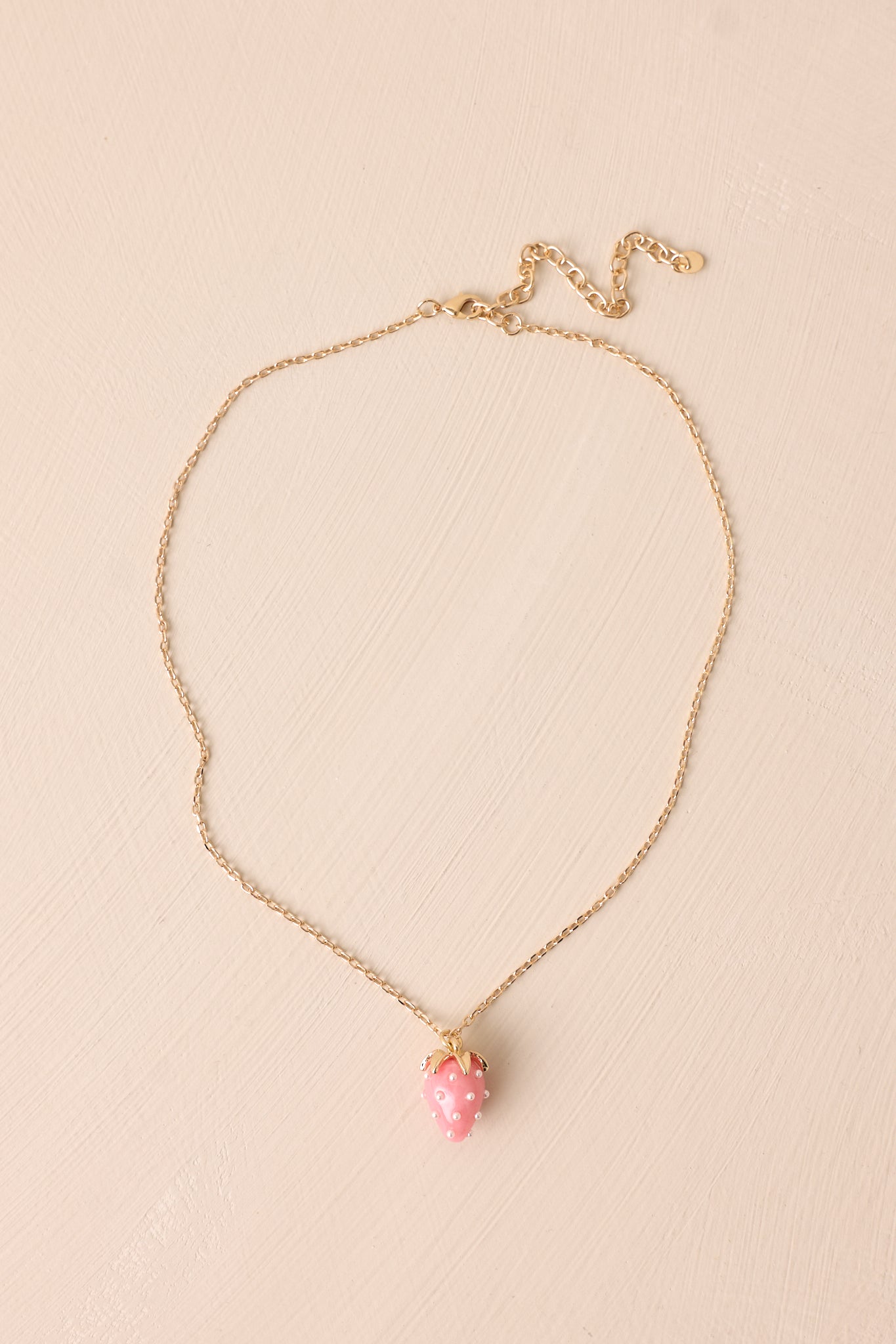 A detailed view of the pink strawberry charm, highlighting its glossy acrylic design, faux pearl accents, and gold chain for a whimsical look.