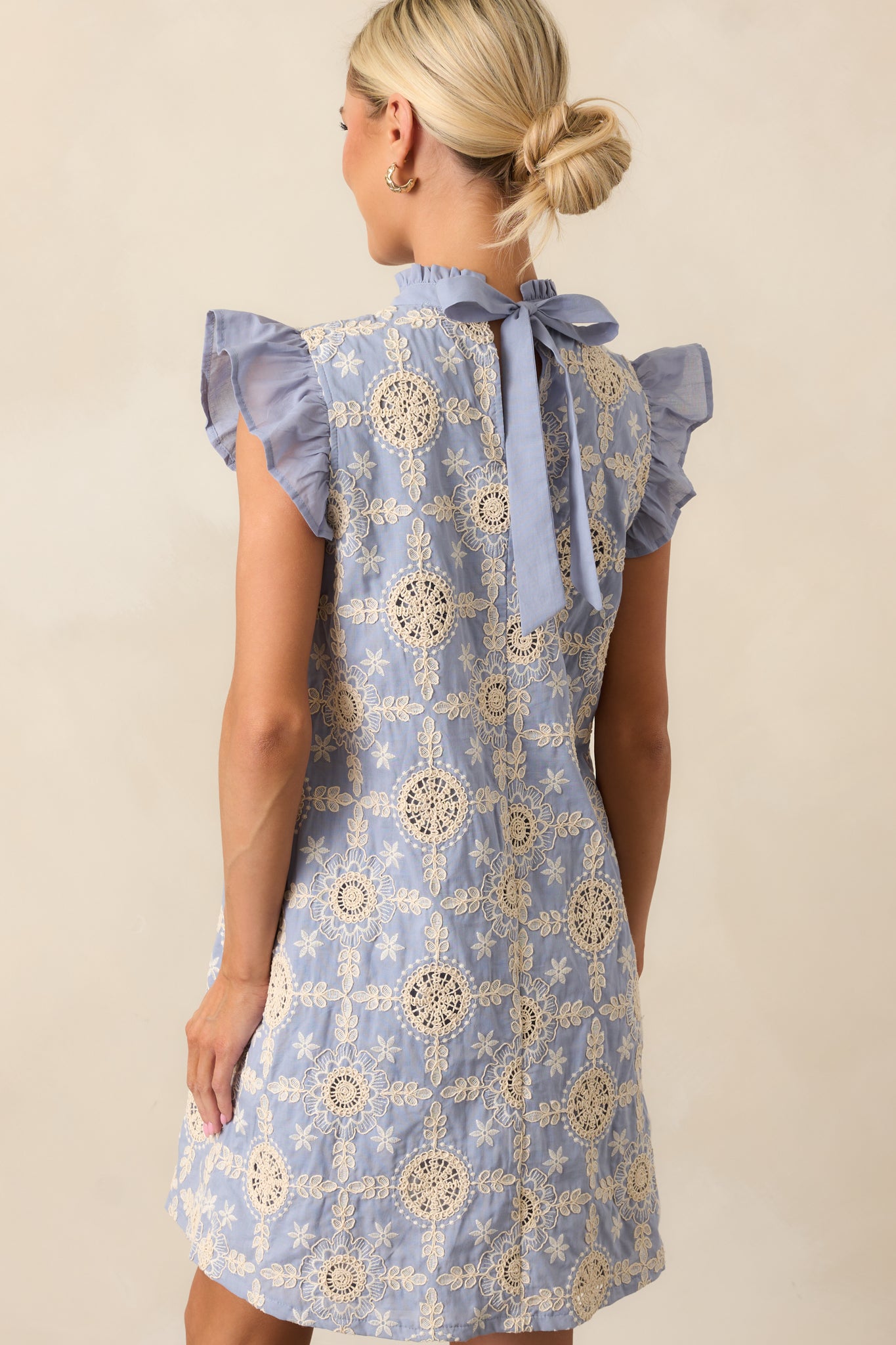 The bow back detail adds a charming, decorative element, complementing the embroidered design and flutter sleeves.