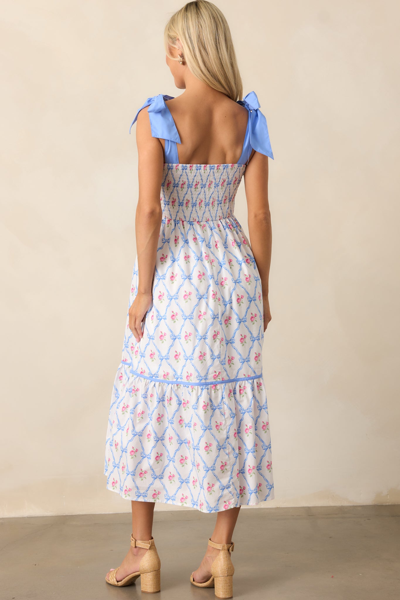 The back view of the blue dress showcases the smocked back detailing, highlighting the self-tie ribbon straps and the relaxed fit of the dress.