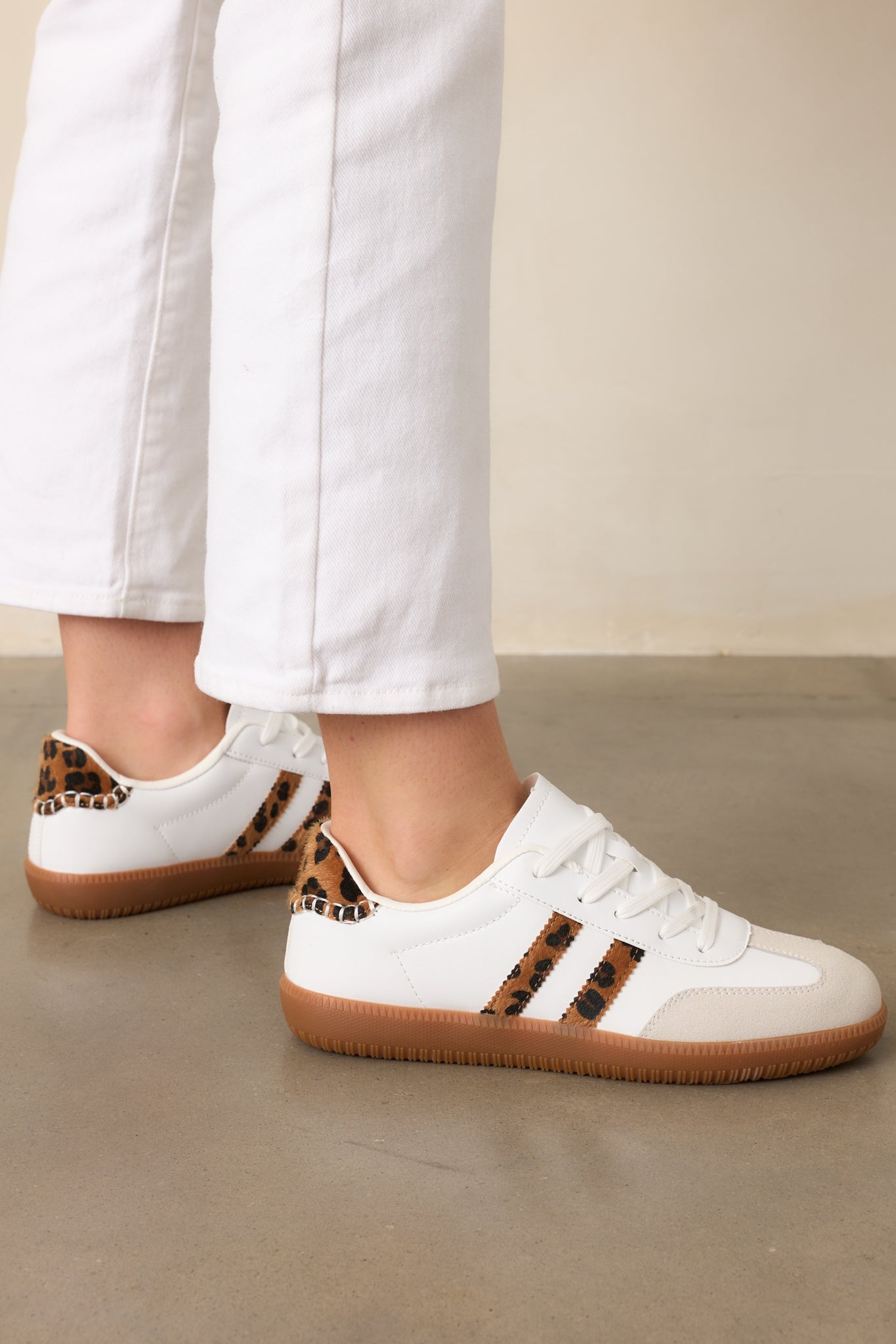 These white sneakers feature a sleek white faux leather material, a round toe, and a brown sole with leopard-colored ricrac faux fur stripes on the side for a stylish and unique touch.