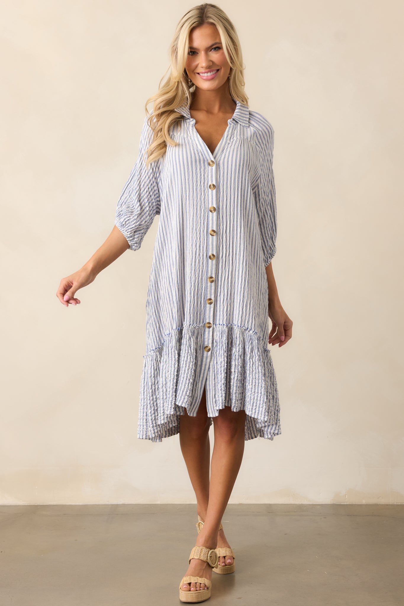 A light blue mini dress with a collared neckline, button front, drop waist detailing, vertical stripes, and short sleeves with elastic cuffs.