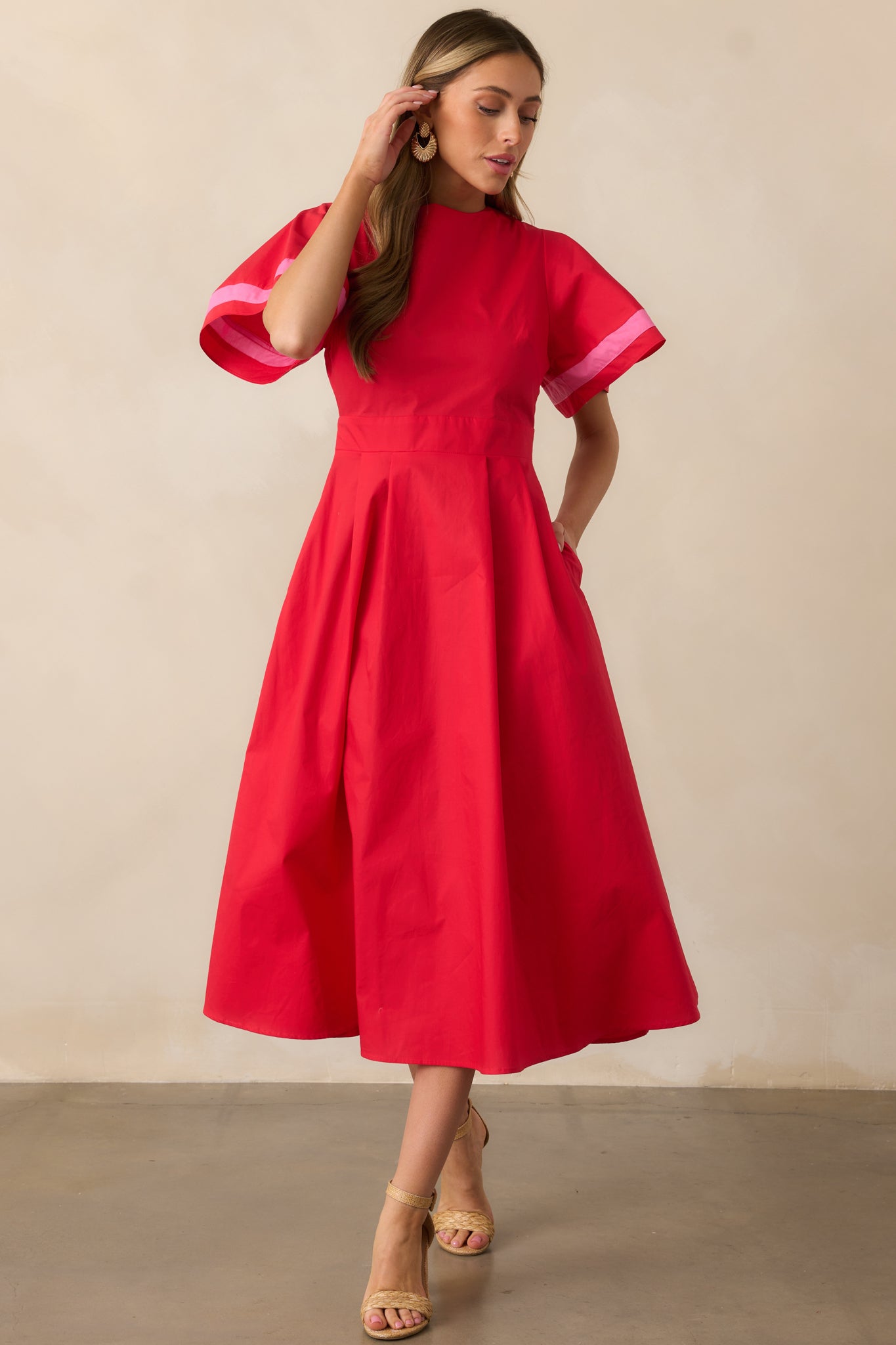 This red dress features a round neckline, soft puffy sleeves with pink striped cuffs, and a waist-hugging fit that accentuates the figure.