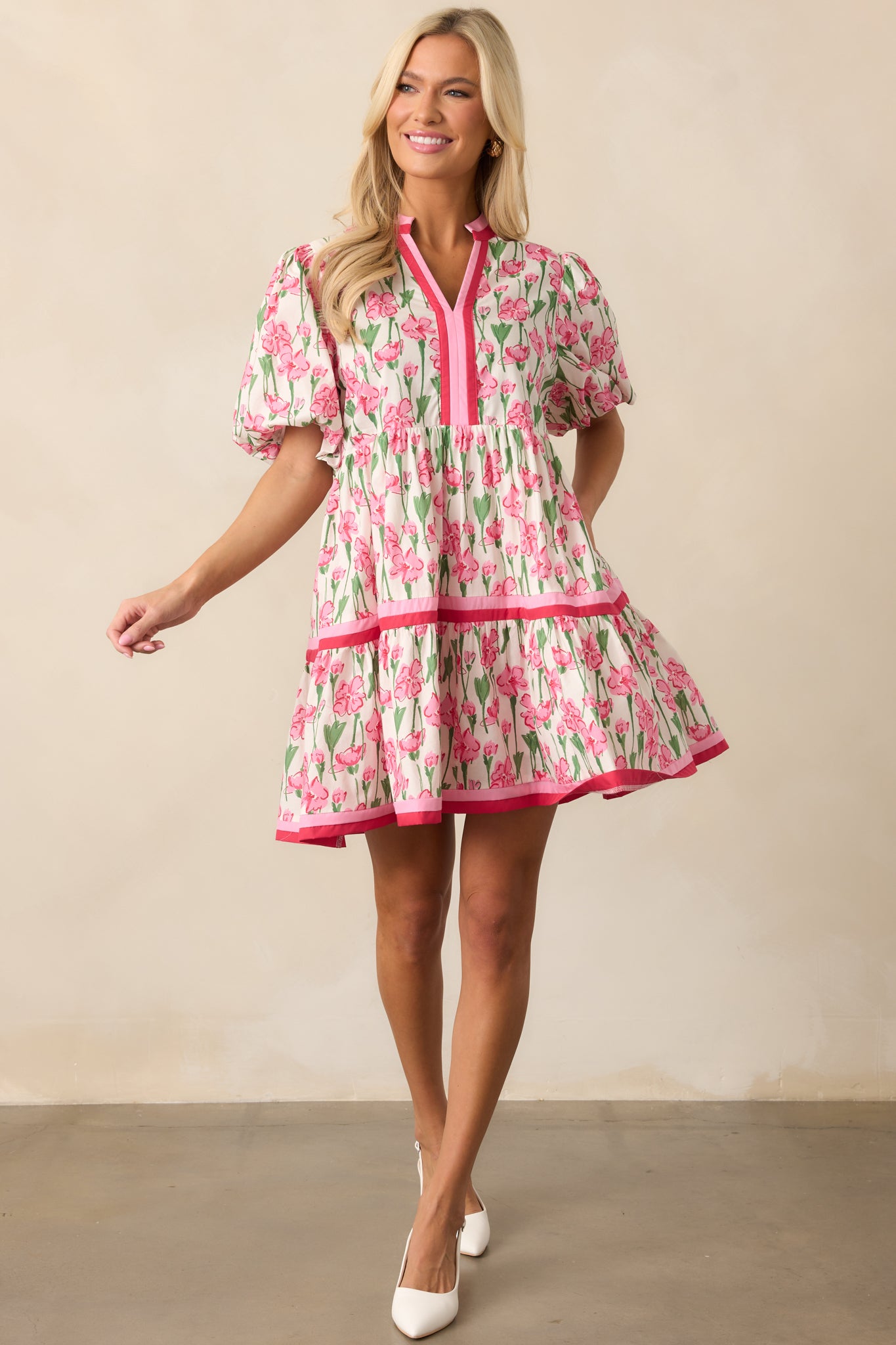 A playful pink dress with puffed sleeves, a V-neckline, and tiered layers, finished with pink stripes along the hems