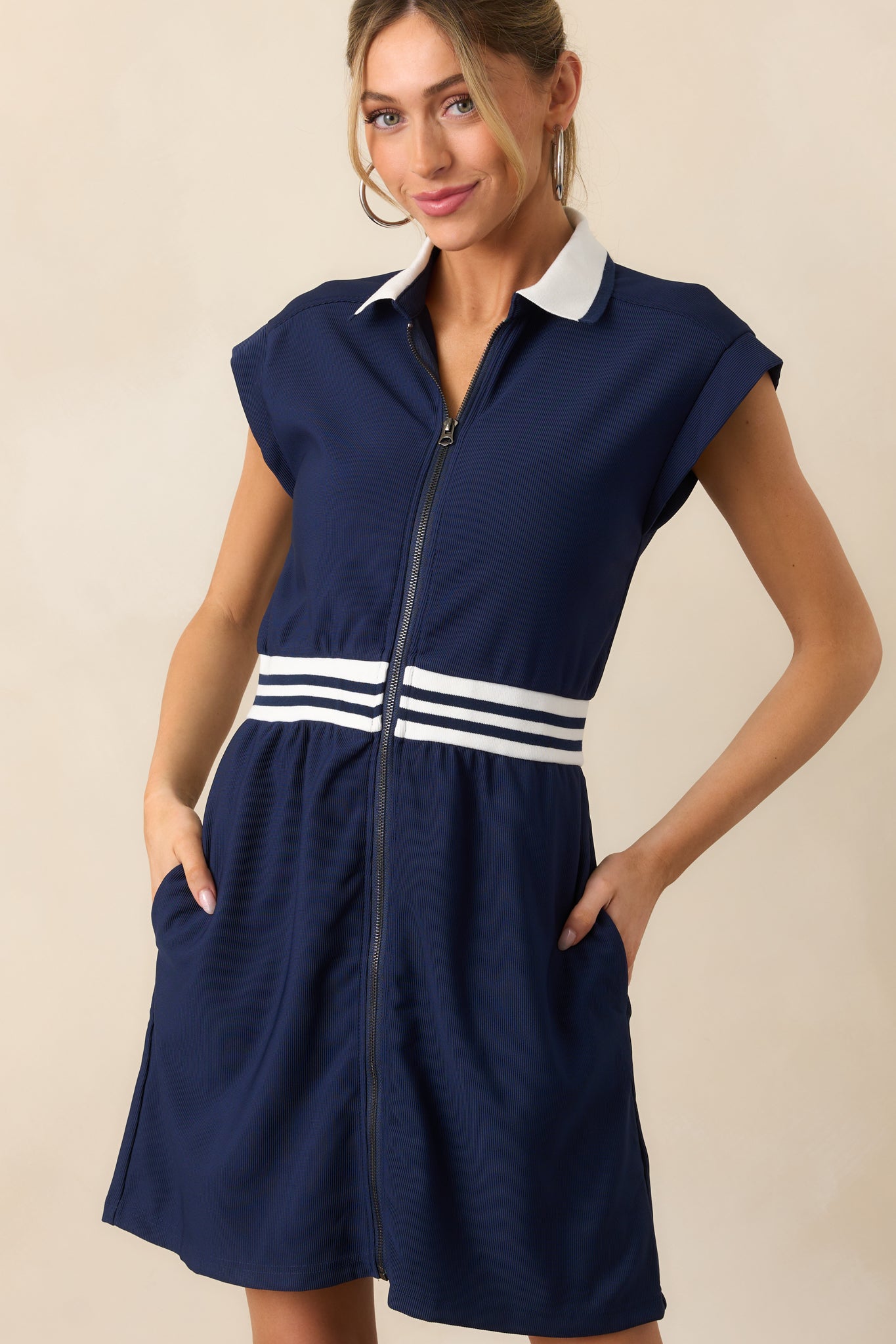 The stripe detailing at the waist creates a flattering, cinched look on this navy dress, highlighted by the functional zipper front.