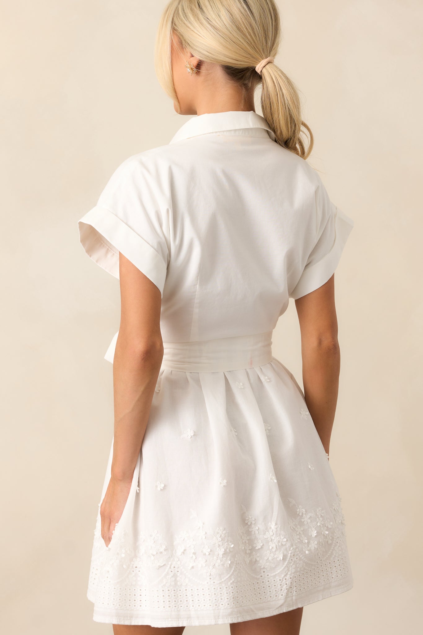 The back of the dress reveals a simple yet elegant design with the self-tie waistband and clean button front, complementing the embroidered hem that adds a unique finish to the piece.