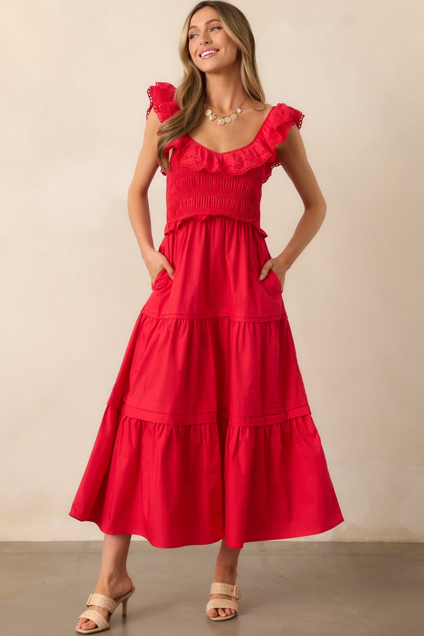 A red maxi dress featuring a ruffled V-neckline, smocked bodice, tiered skirt, and sleeveless design.