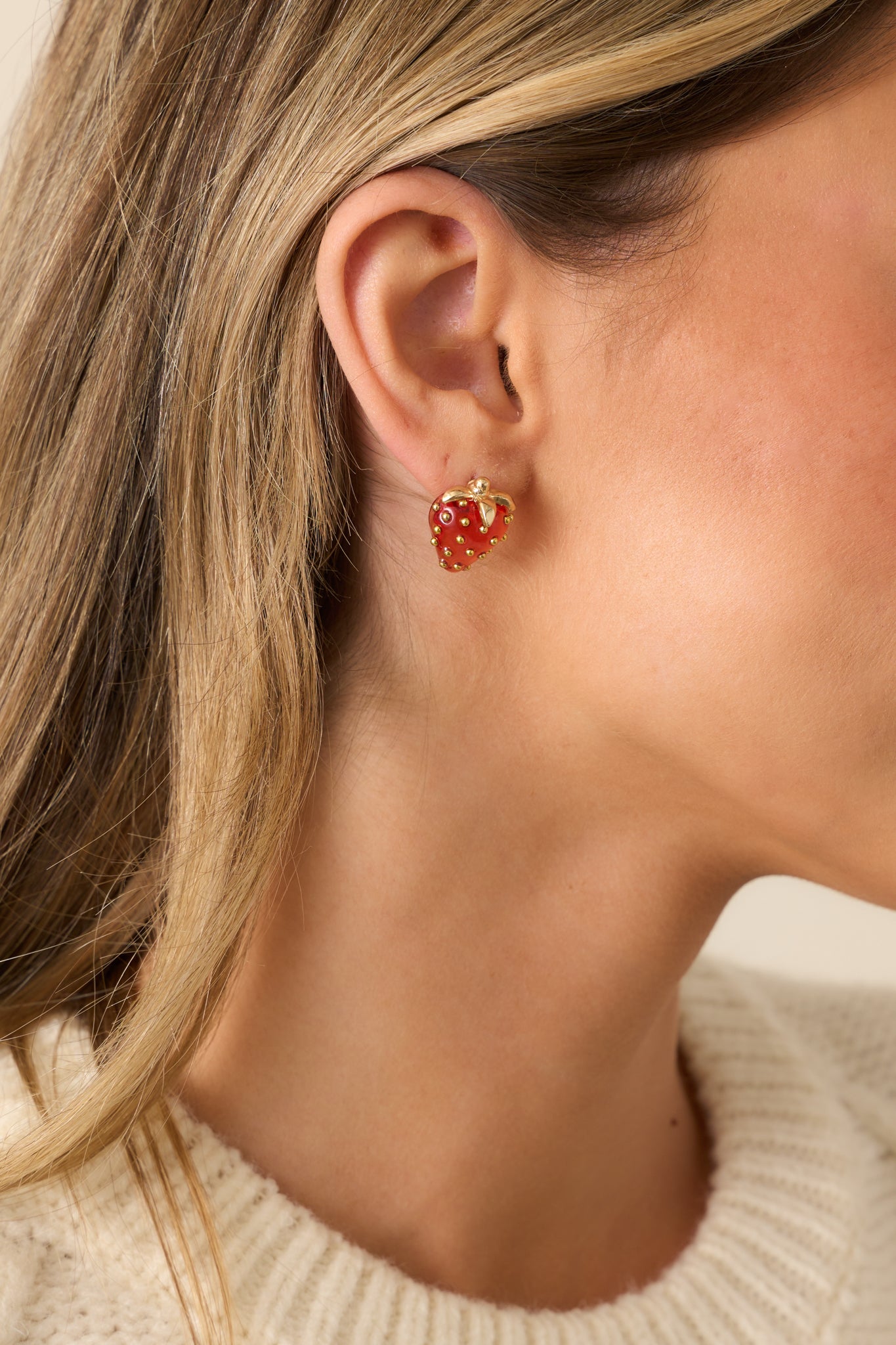 A pair of red strawberry earrings with a 3D clear red resin strawberry, gold hardware, and a stud design.