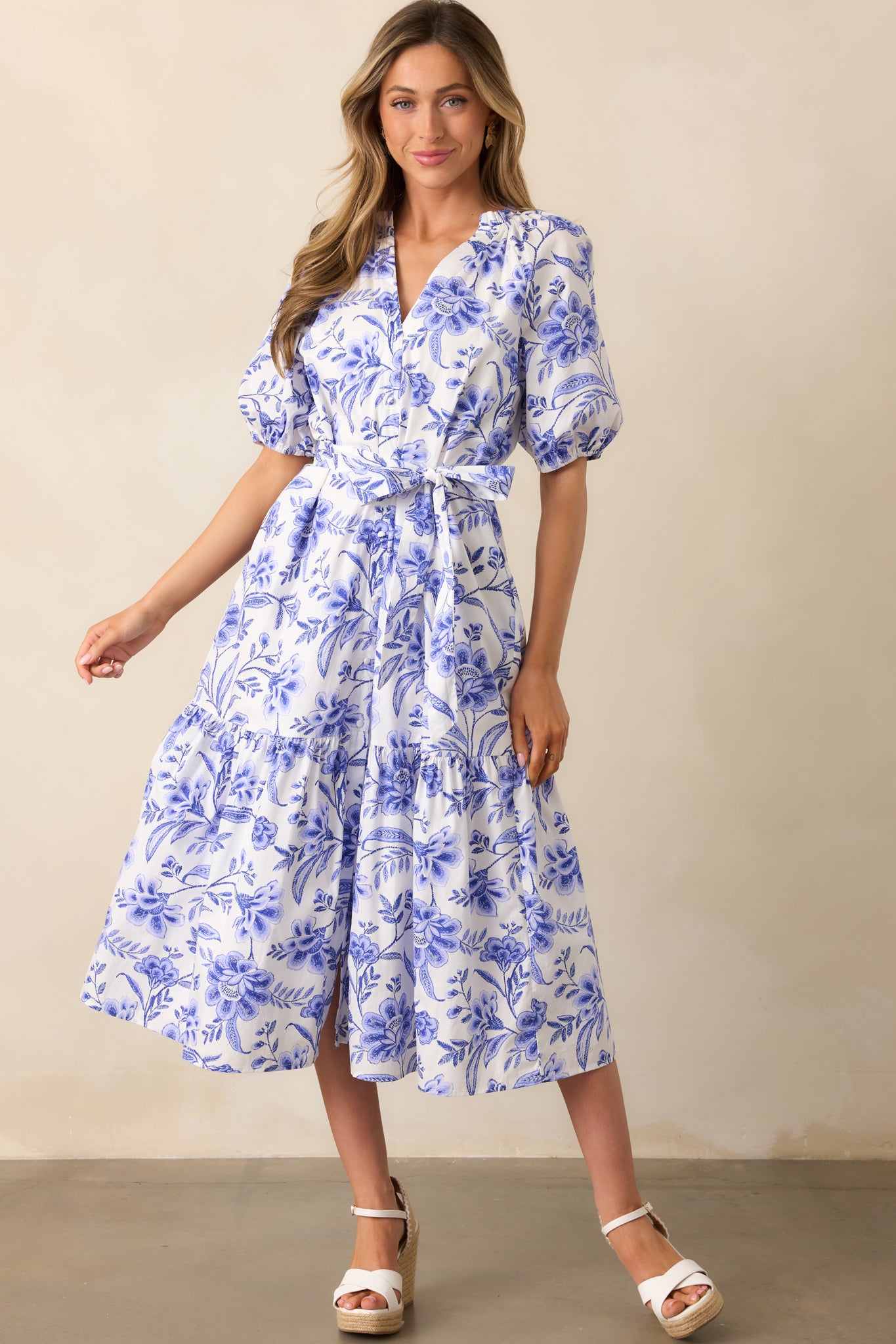 A blue dress with a V-neckline, button front design, self-tie waistband, floral print, and short sleeves.