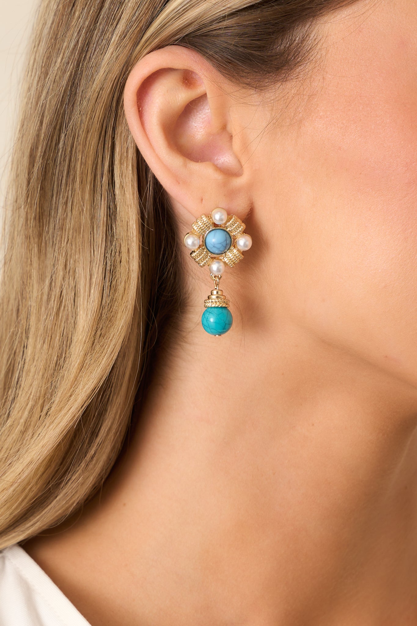 A turquoise center stone is framed by textured gold hardware and ivory faux pearls, creating a classic design.