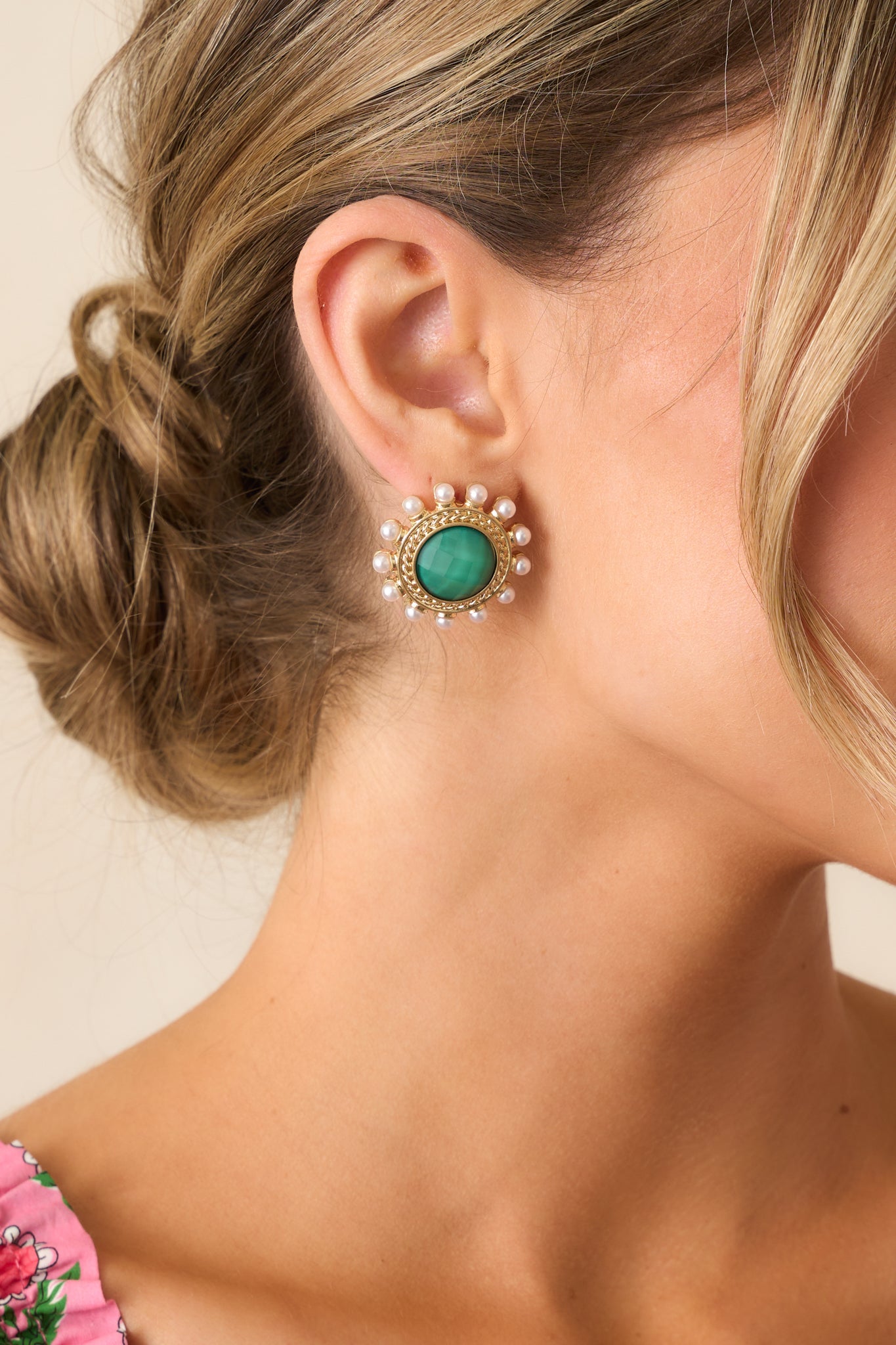 These green and gold earrings showcase a bold circular design with a pearlescent green middle, gold braided border, and ivory faux pearls, adding elegance to any look.