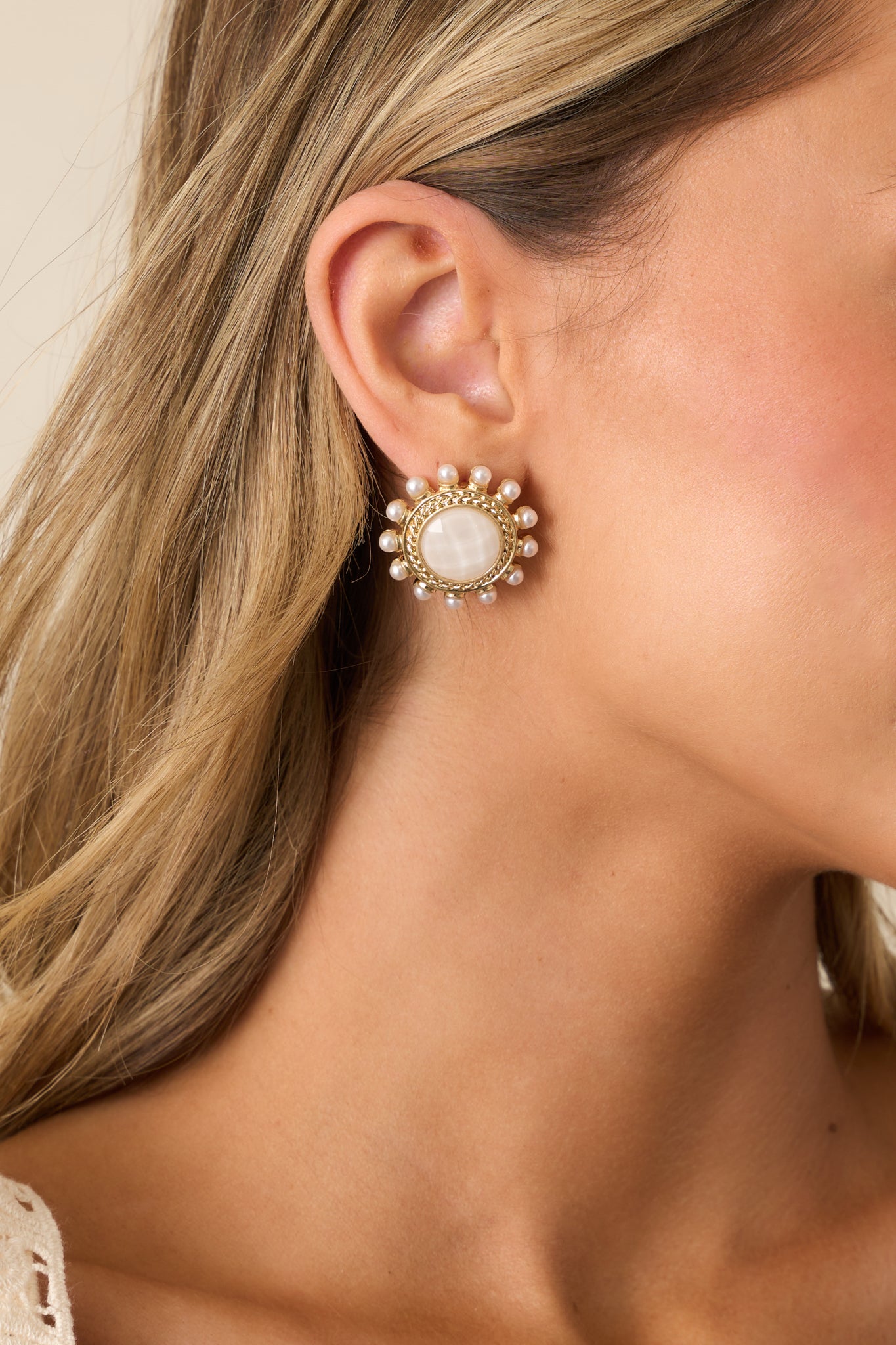 White and gold earrings featuring a large circular shape with a pearlescent white center, framed by a braided gold border and ivory faux pearls.