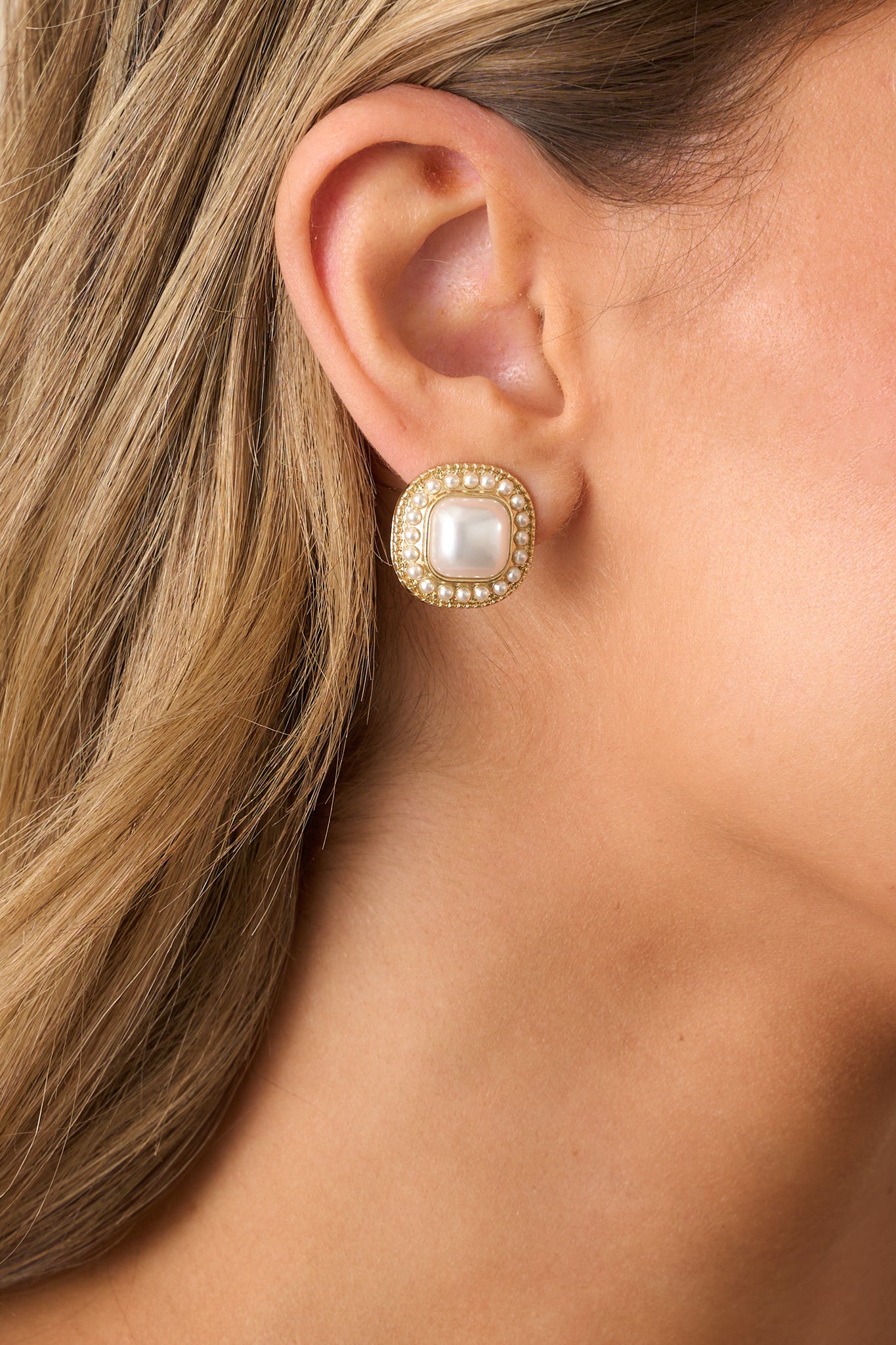 A detailed view of gold square earrings with a textured gold finish, showcasing the large faux ivory pearl in the center surrounded by small ivory pearls.