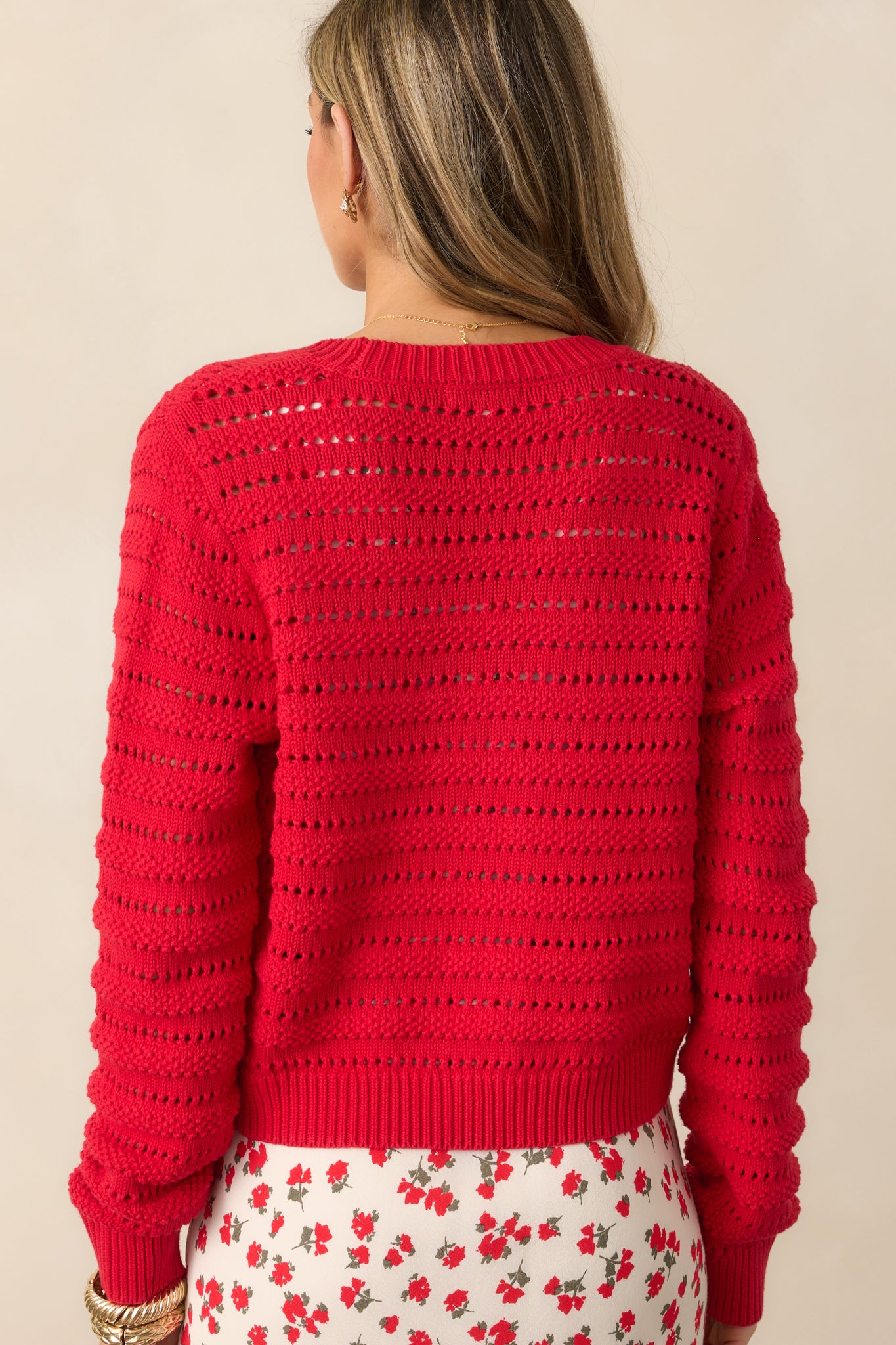 A back view of the red cardigan, showcasing the smooth fabric, open stitch design, and ribbed detailing at the bottom and on the sleeves.