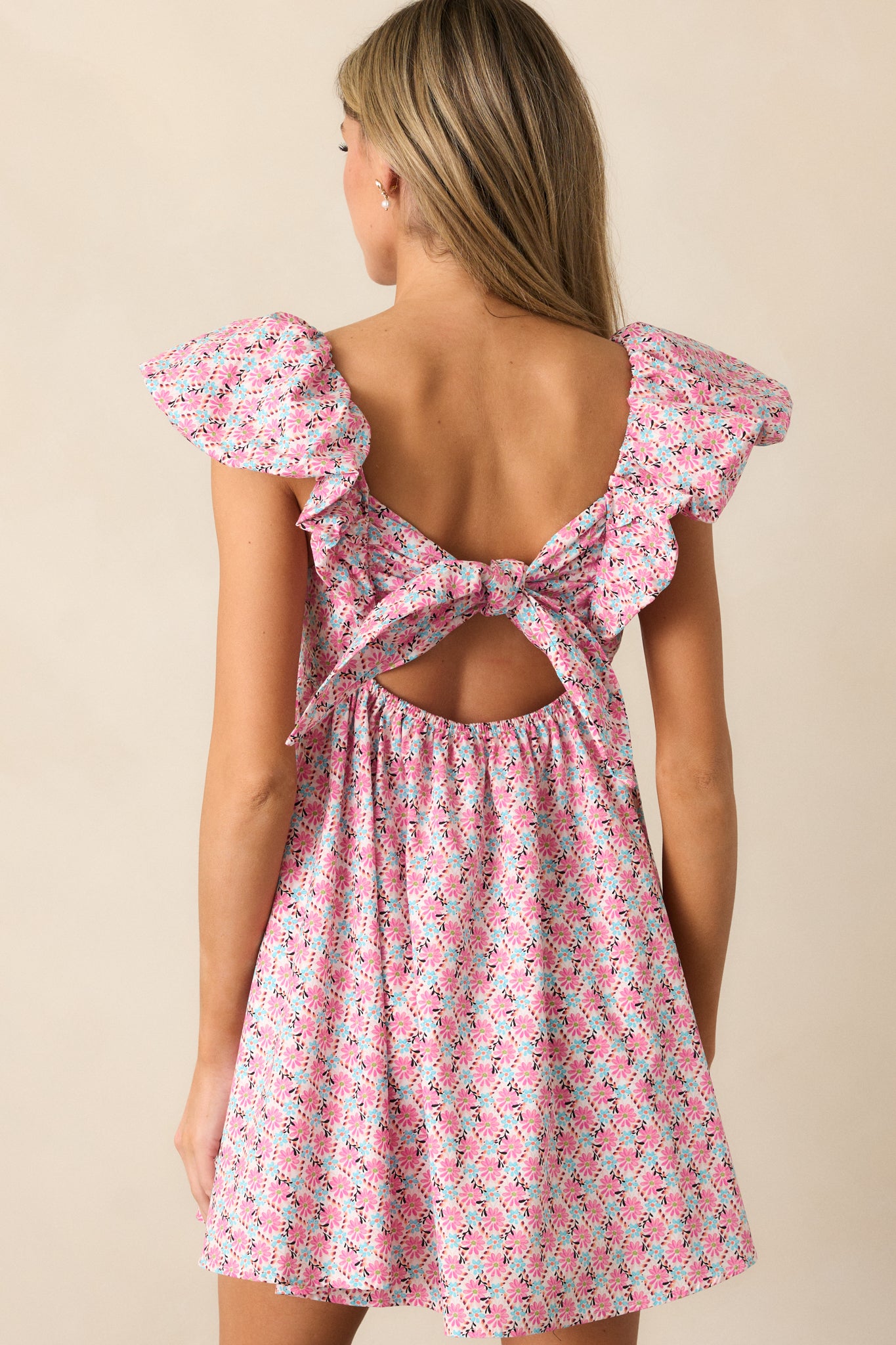 The back of the pink floral dress reveals the self-tie feature and elastic waistband, while the flutter sleeves and babydoll cut create a flattering, feminine silhouette