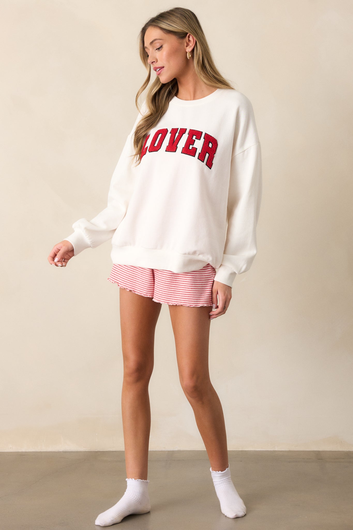 A side view showcasing the relaxed fit of the ivory sweatshirt and the ribbed cuffs on the sleeves, with a clear focus on the "LOVER" script detail.