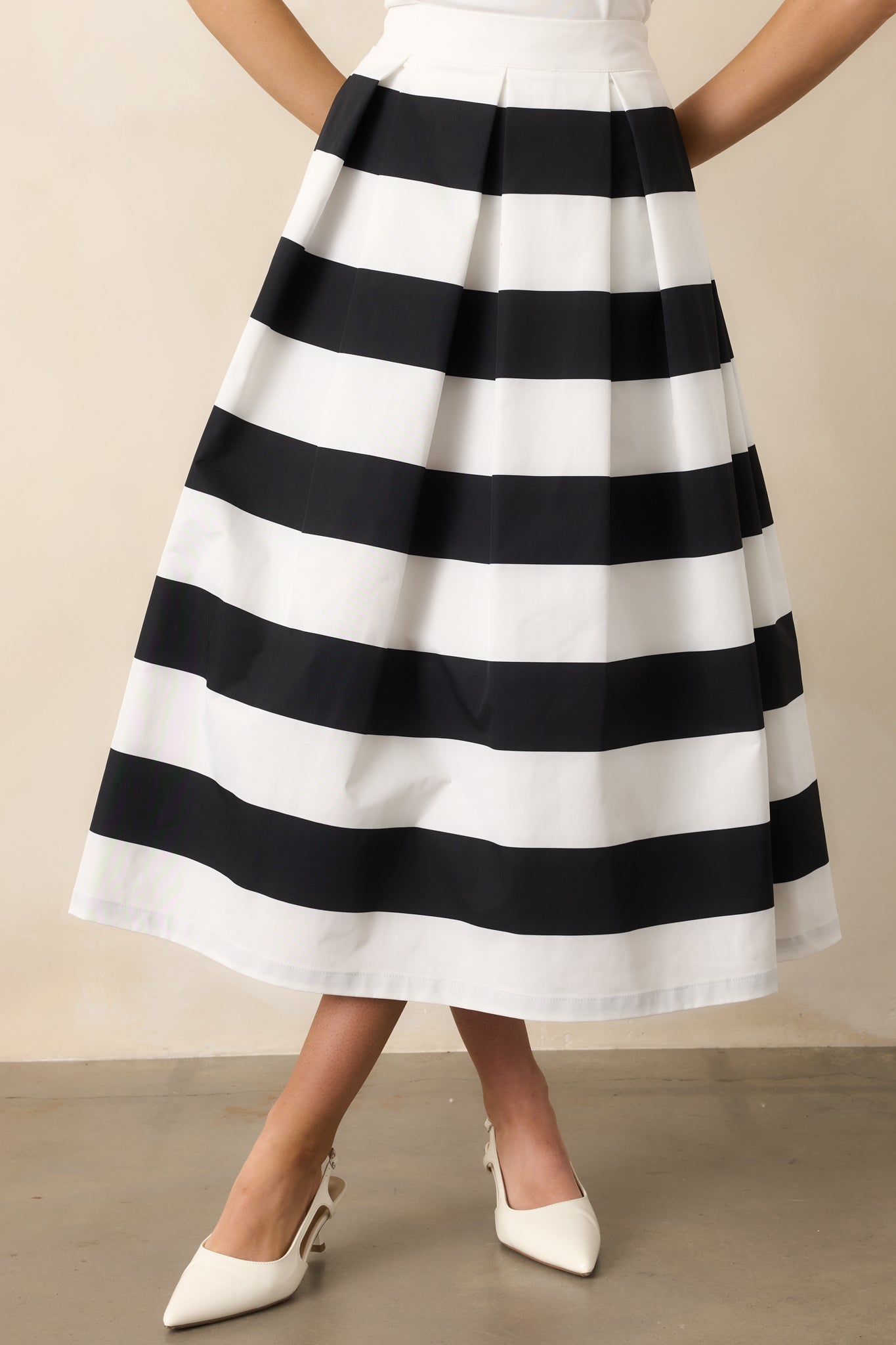 Front view of a black & white midi skirt featuring a high waisted design, a discrete side zipper, a thick waistline and functional hip pockets.