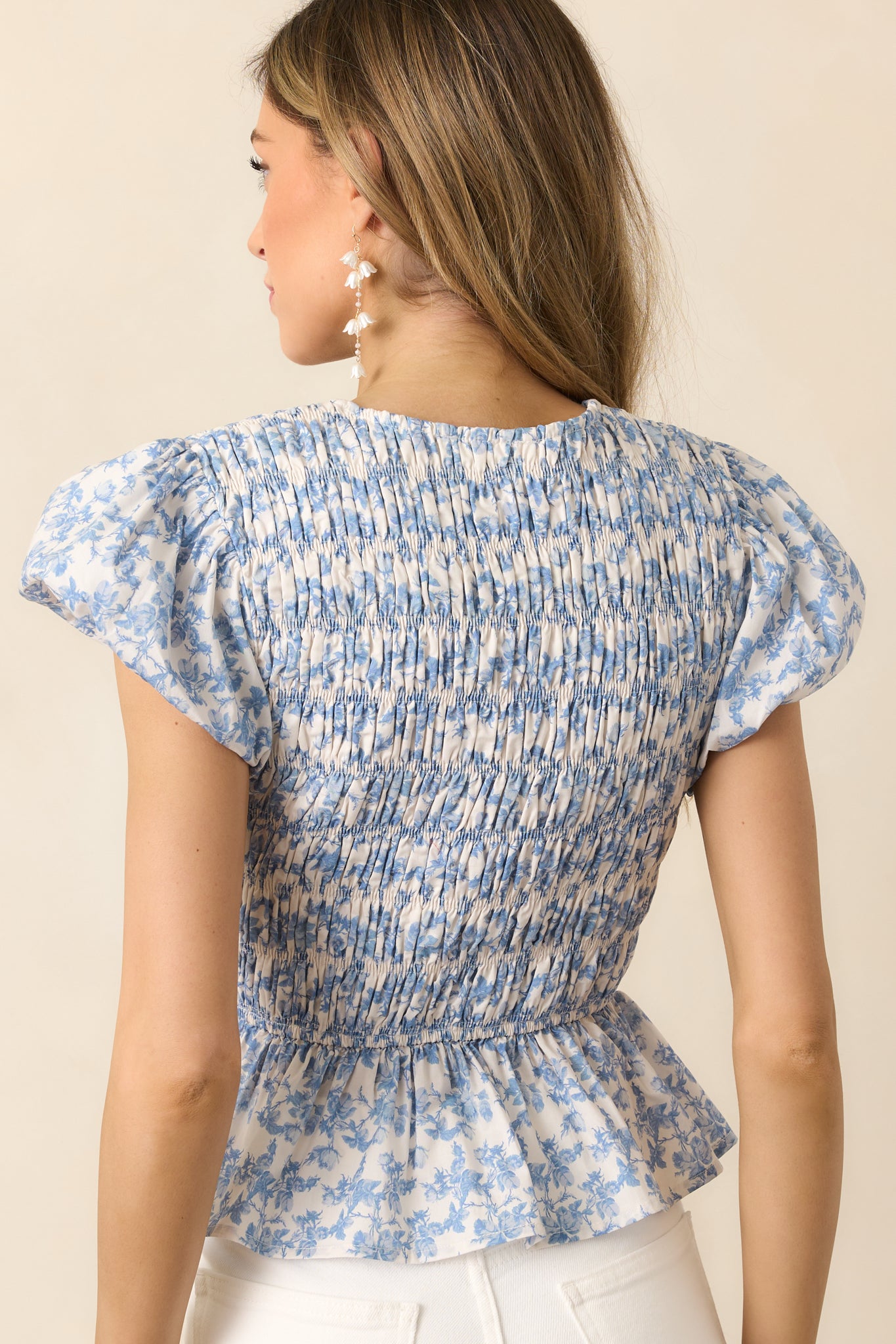 A back view of the blue top, showcasing the smocked bodice and flutter sleeves, with the peplum hem adding a soft, flared finish.