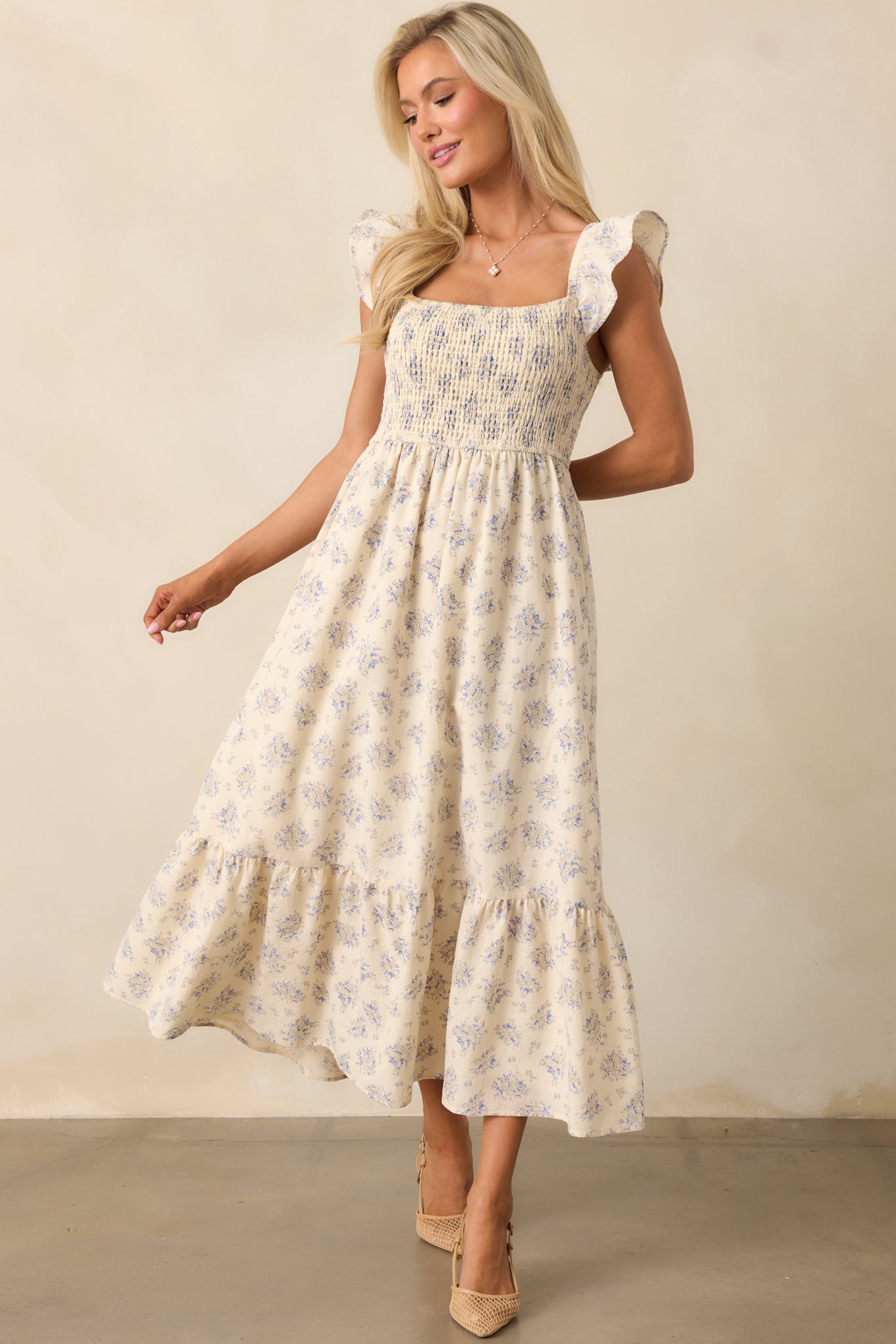 A beige dress featuring flutter sleeves, a fully smocked bust, and a flowing tiered skirt for a soft, romantic look.