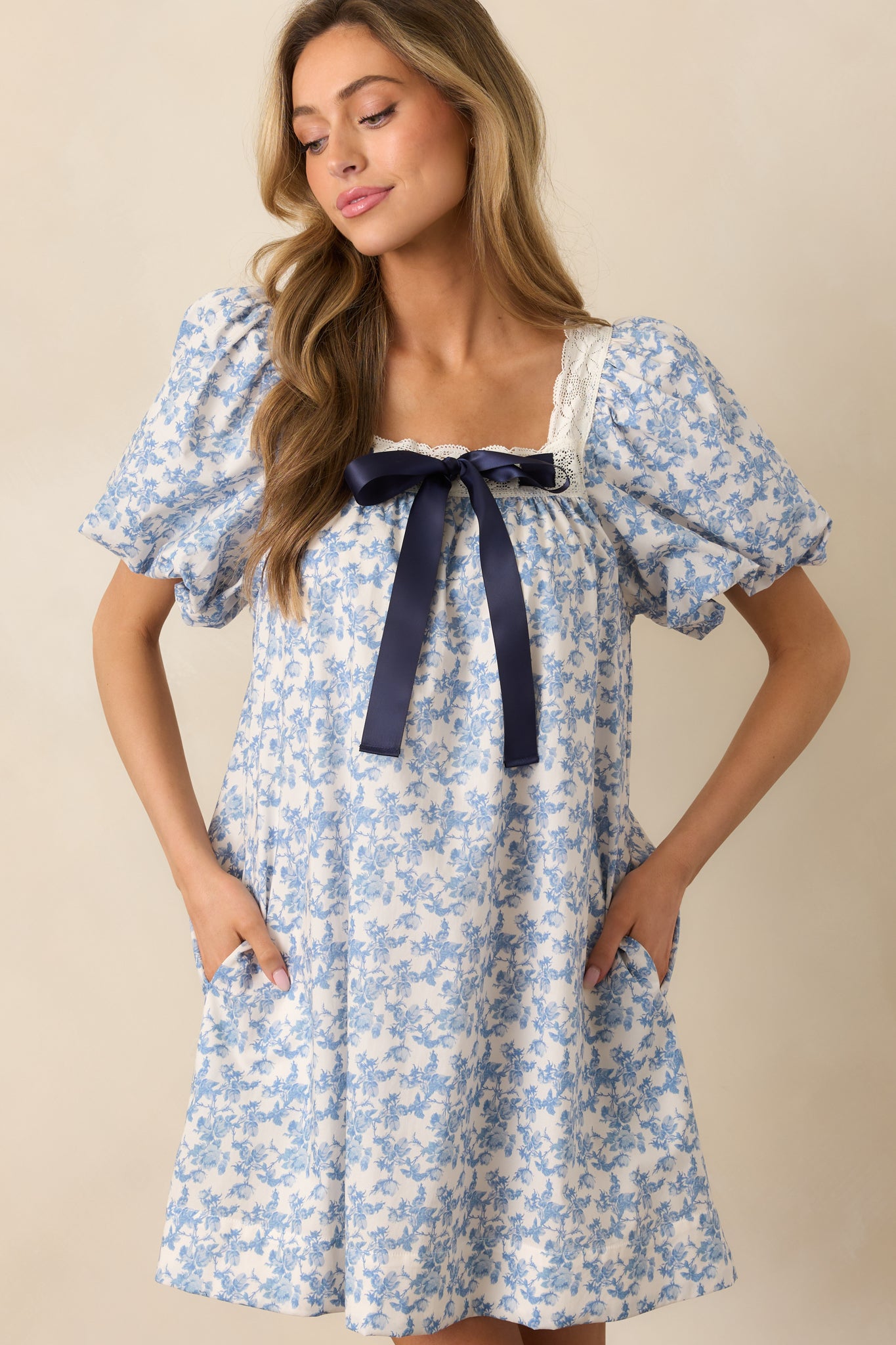 A cropped view showing the square neckline and self-tie satin navy bow at the waist of the blue mini dress, with a glimpse of the functional side pockets.