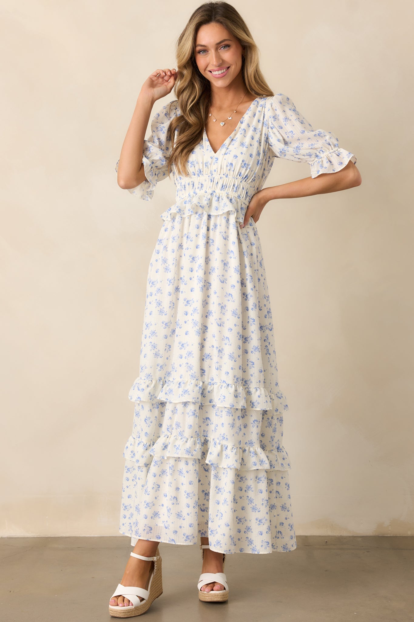  A breezy ivory dress featuring a v-neck neckline, ruffle details, and a delicate blue floral pattern throughout.