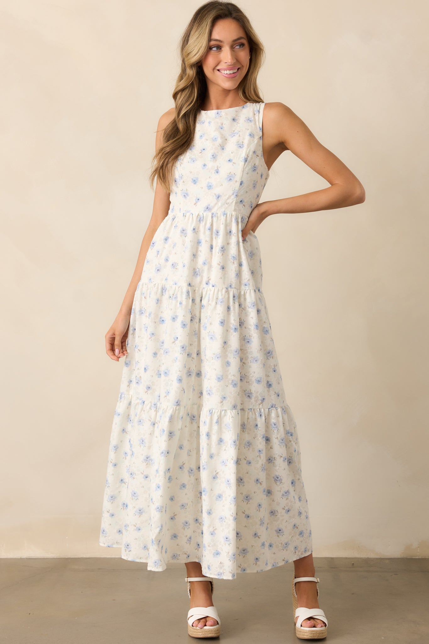 A soft, airy ivory dress with a blue floral pattern, showcasing its round neckline and cascading three-tiered design.