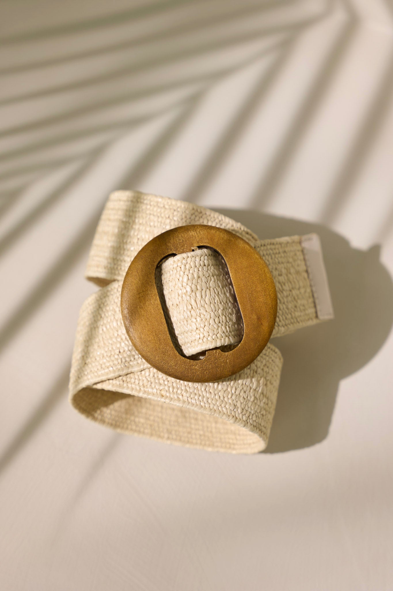 A partial view of the ivory belt, highlighting the woven straw material and the large wooden circular buckle at the center.