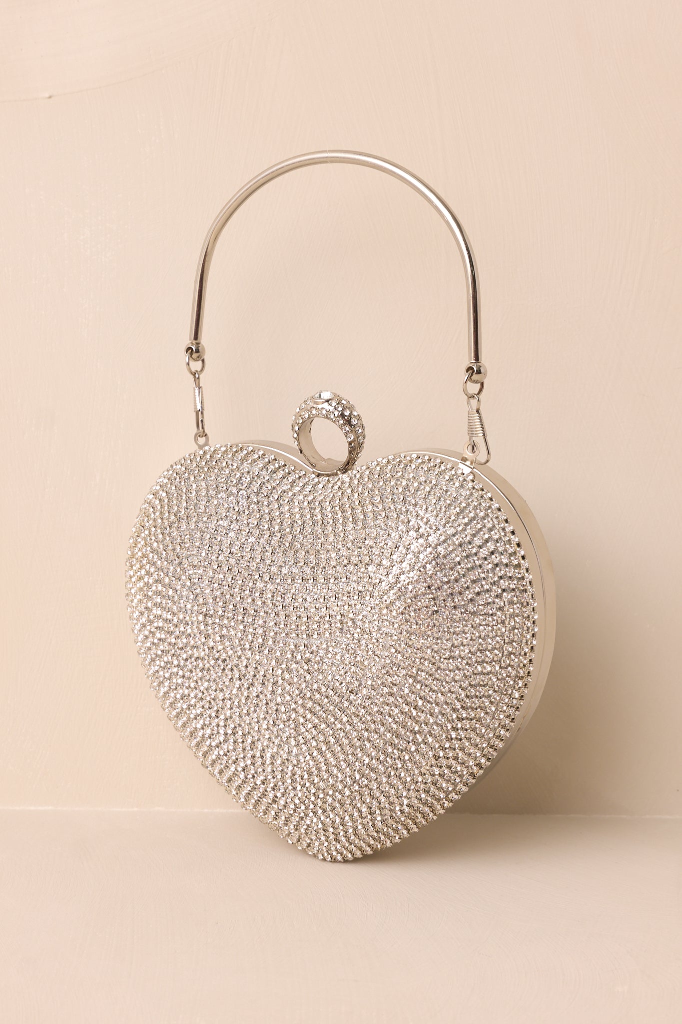 An angled side view of the silver clutch showing its heart shape, metallic silver back, and silver ring handle.