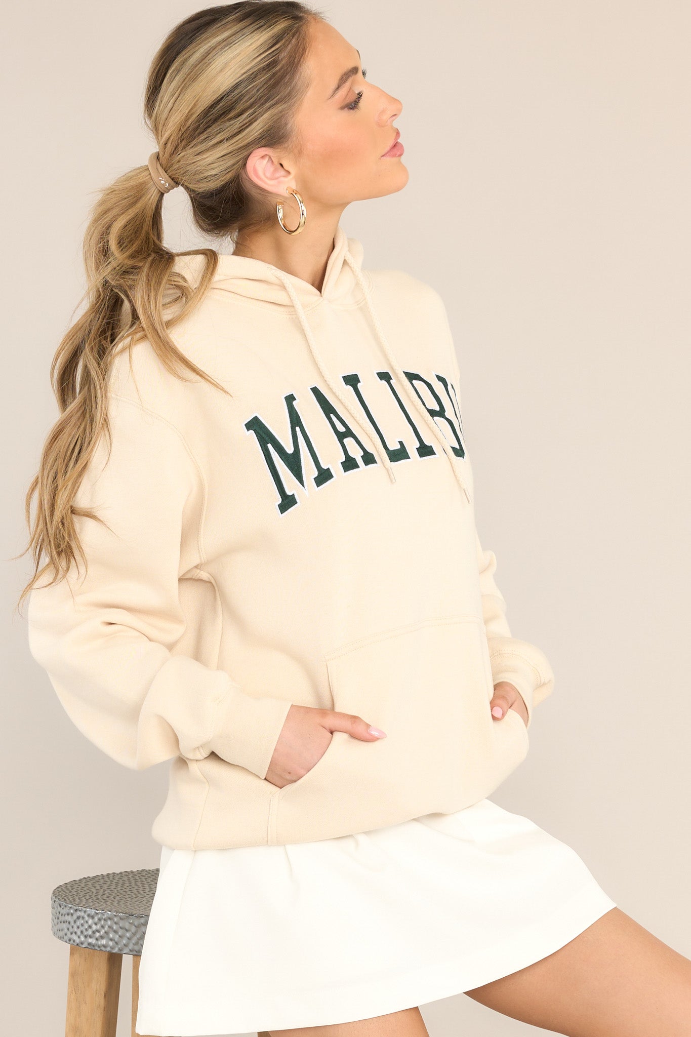 This natural colored hoodie features embroidered "Malibu" text, a drawstring hood, a kangaroo pocket, and a relaxed fit.