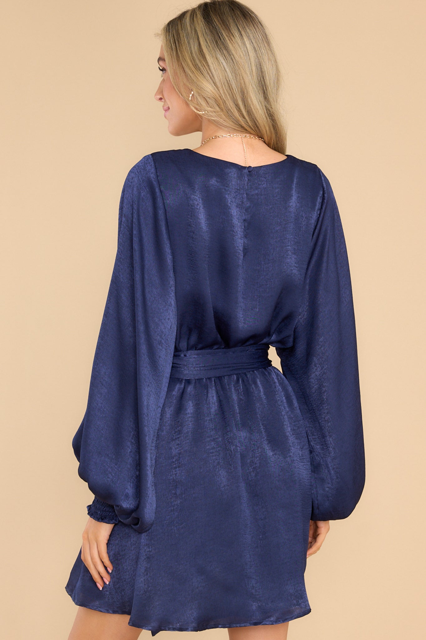 Back view of this dress that features a round neckline, a keyhole with a button closure on the back, flowy sleeves with smocked cuffs, an elastic waistband, a self-tie, and a flowy skirt.