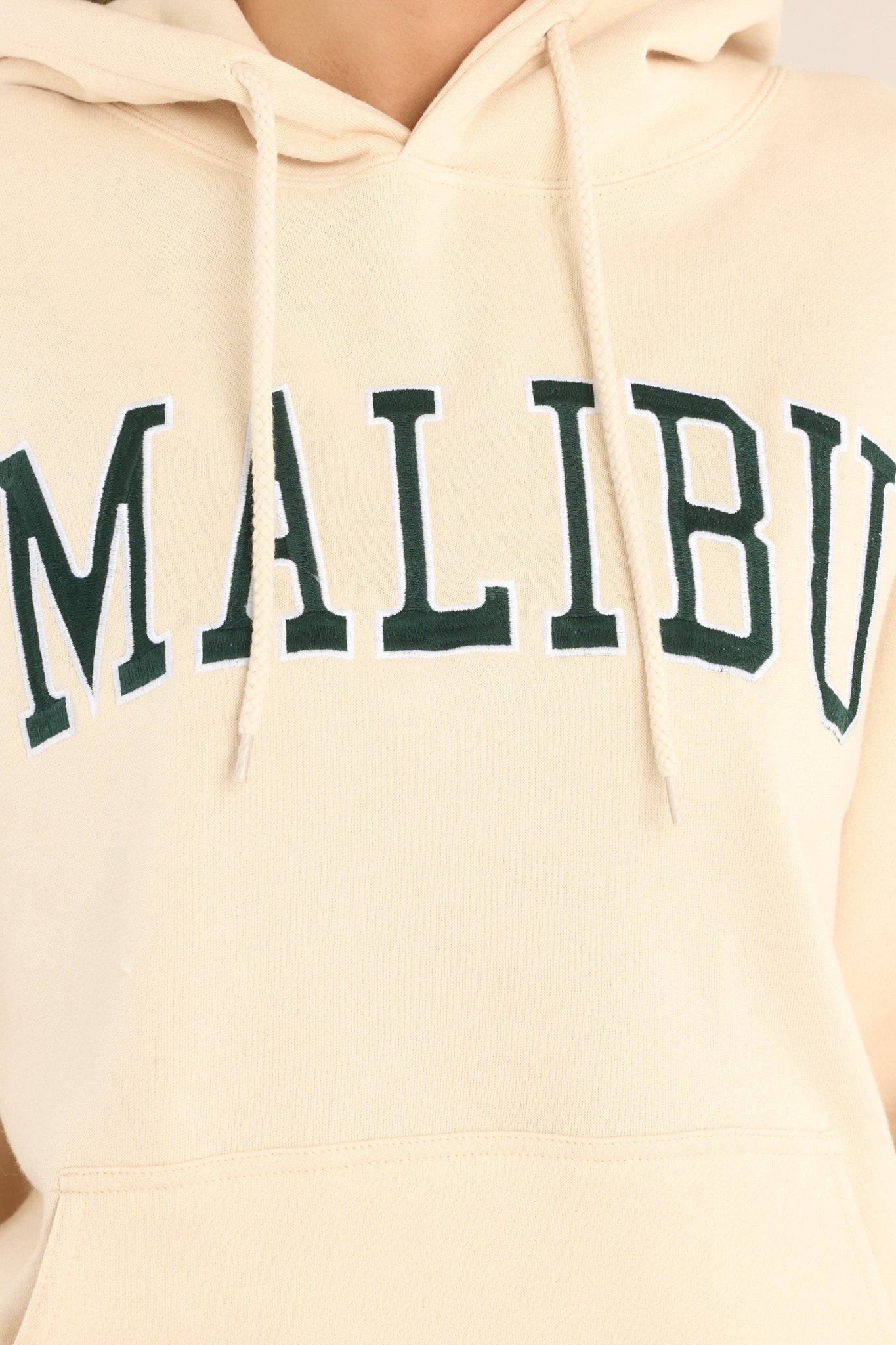 Close up view of this hoodie that features embroidered "Malibu" text, a drawstring hood, a kangaroo pocket, and a relaxed fit.