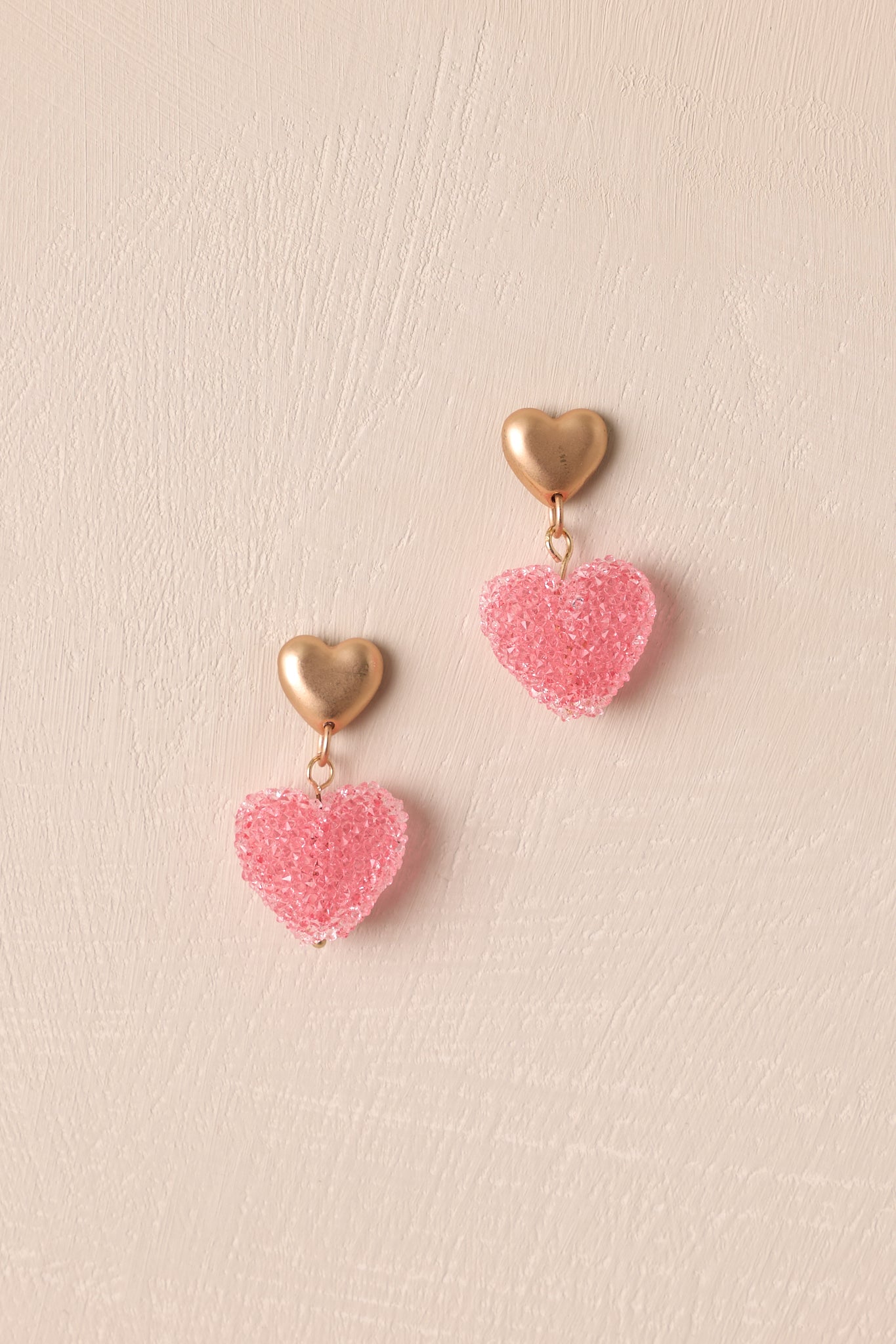 A close-up of the earrings, showcasing the matte gold heart stud, connecting gold jump rings, and the pink faux sugar-coated gumdrop heart at the bottom.