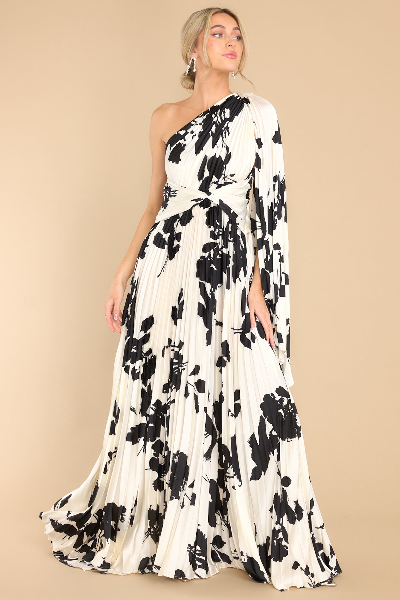 This ivory and black dress features an asymmetric neckline, fabric trailing from the shoulder, twisted detailing in the waist, and pleats throughout.