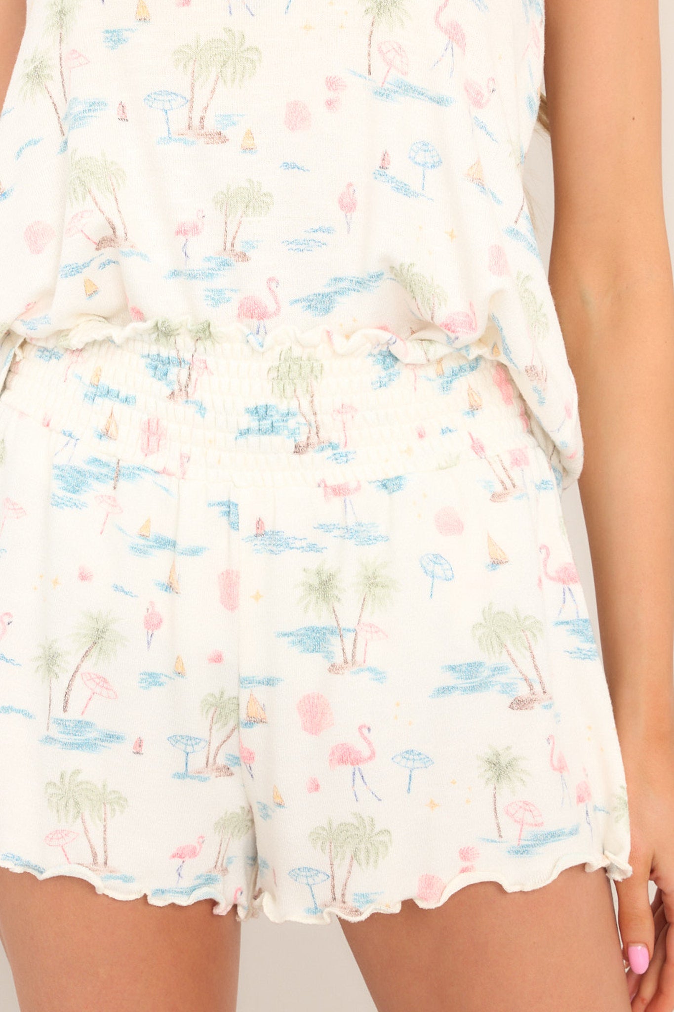 Close up view of these shorts that feature a high waisted design, a fully smocked waistband, a super soft &amp; lightweight material, a tropical print, and a lettuce trim hemline.