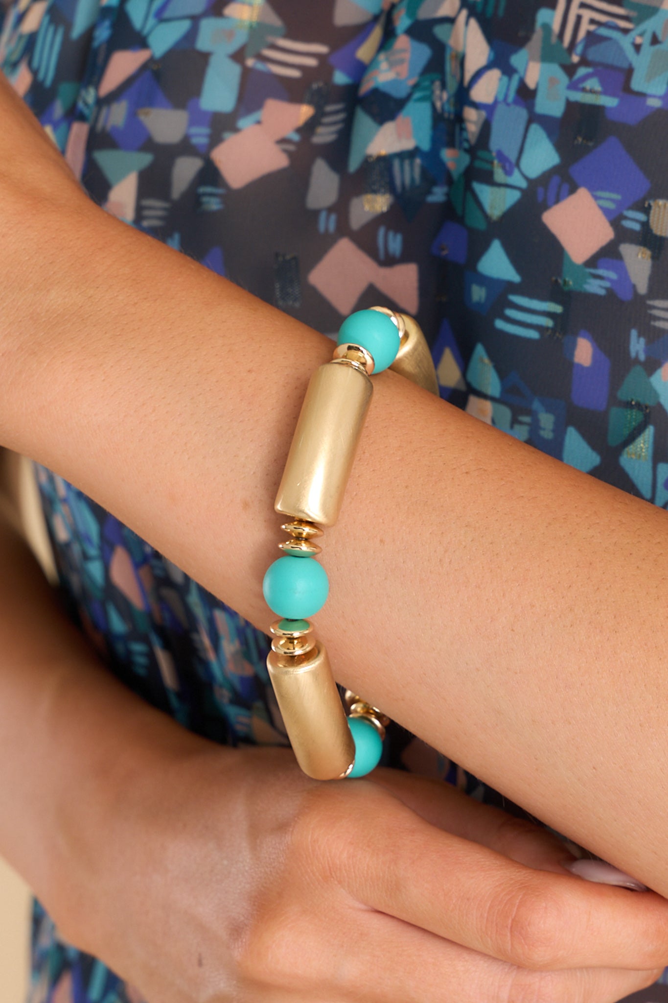 Model shown wearing bracelet that features alternating gold and teal beads. 