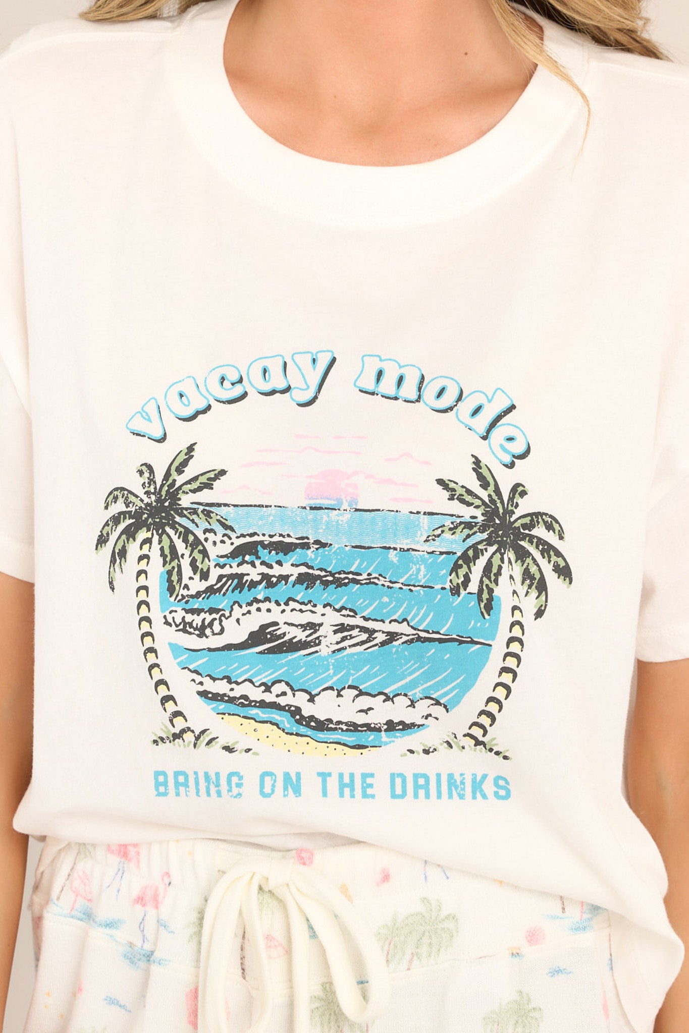 Close up view of this tee that features a crew neckline, dropped shoulders, a tropical graphic, a slightly cropped length, a split hemline, and short sleeves.