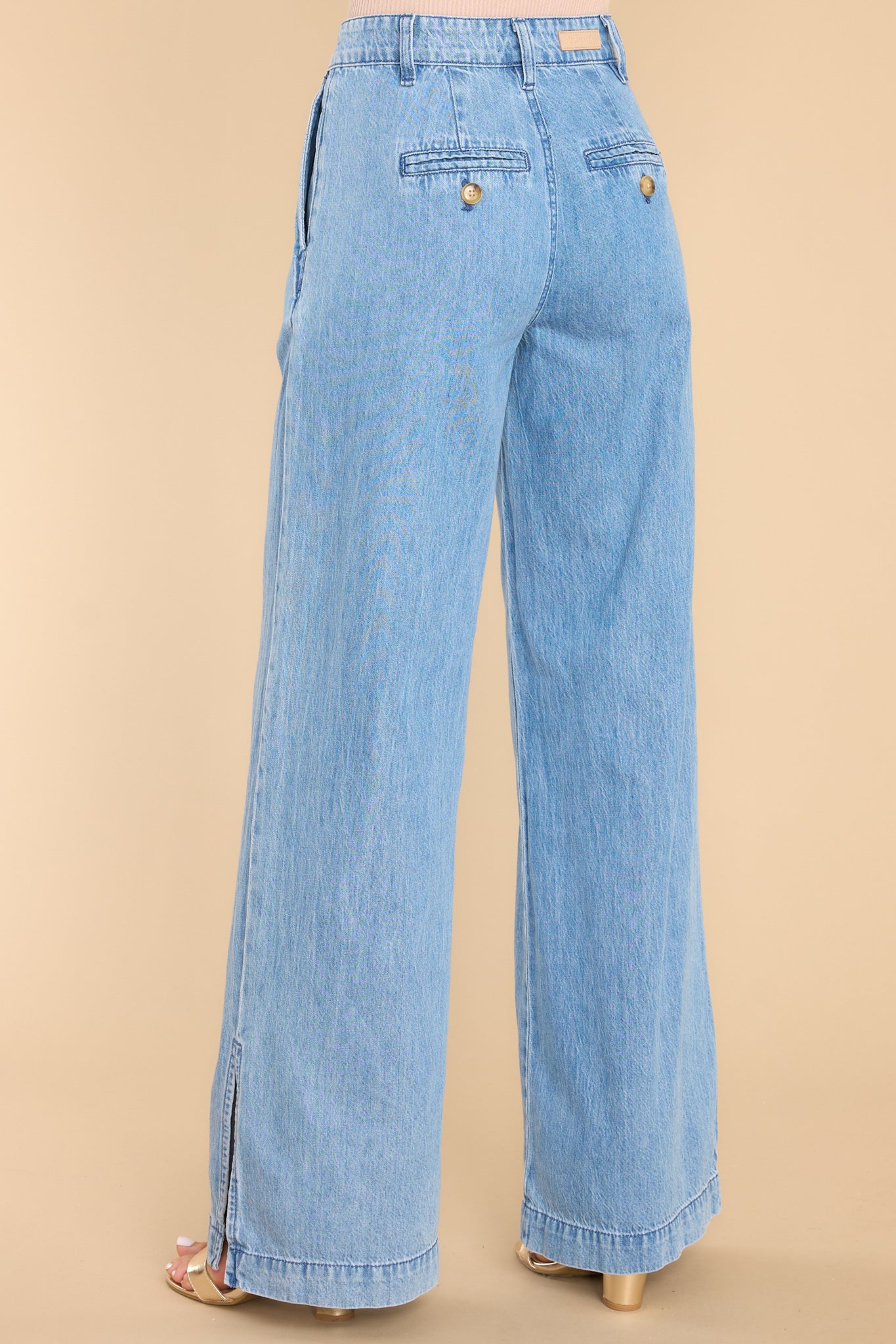 Back view of these pants that feature a high rise waist, a functional zipper, four functional pocket detailing, and a wide leg with side slits.