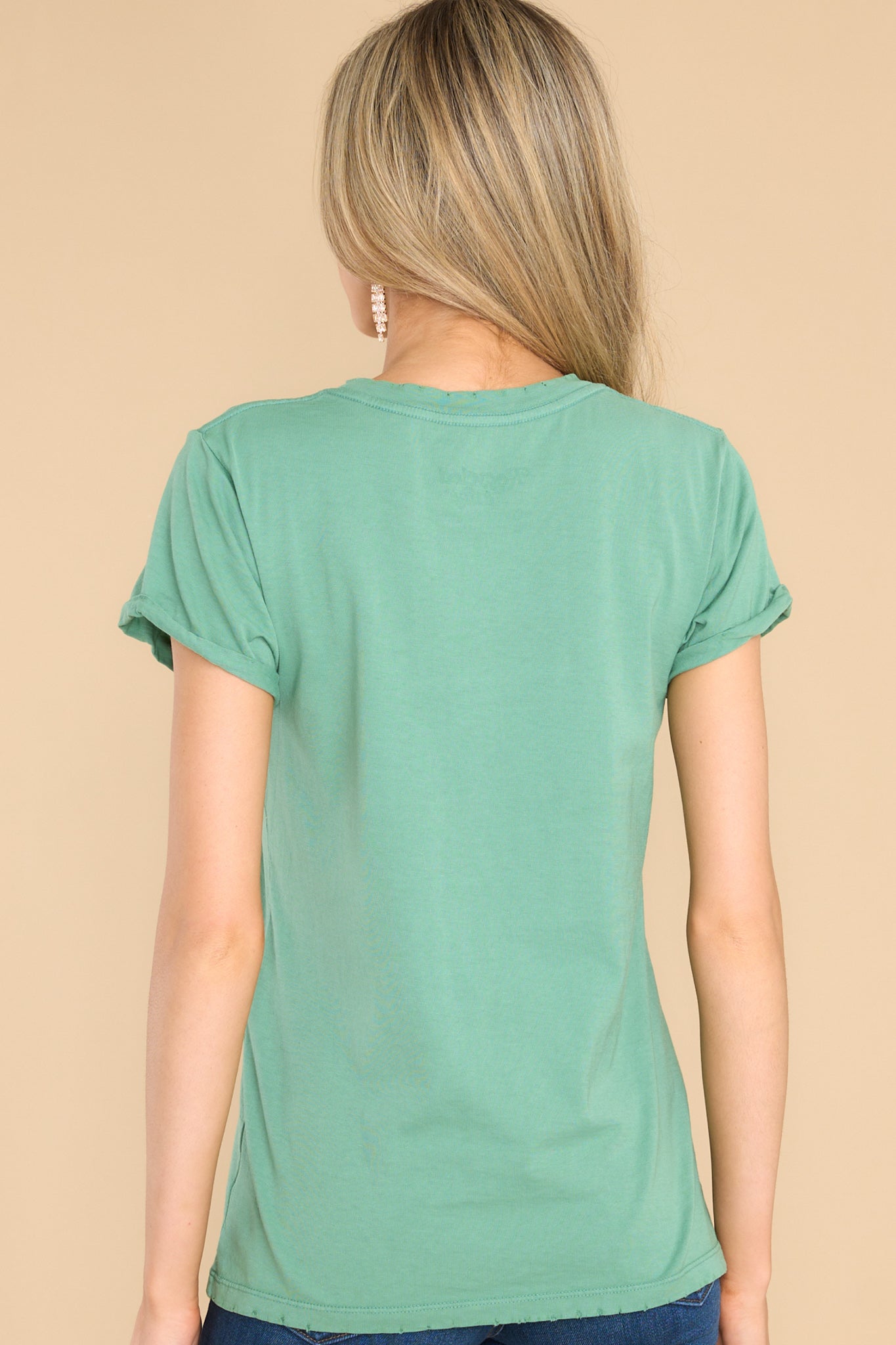 Back view of this tee that features a distressed crew neckline, short folded sleeves, and distressed detailing along the bottom hem. 