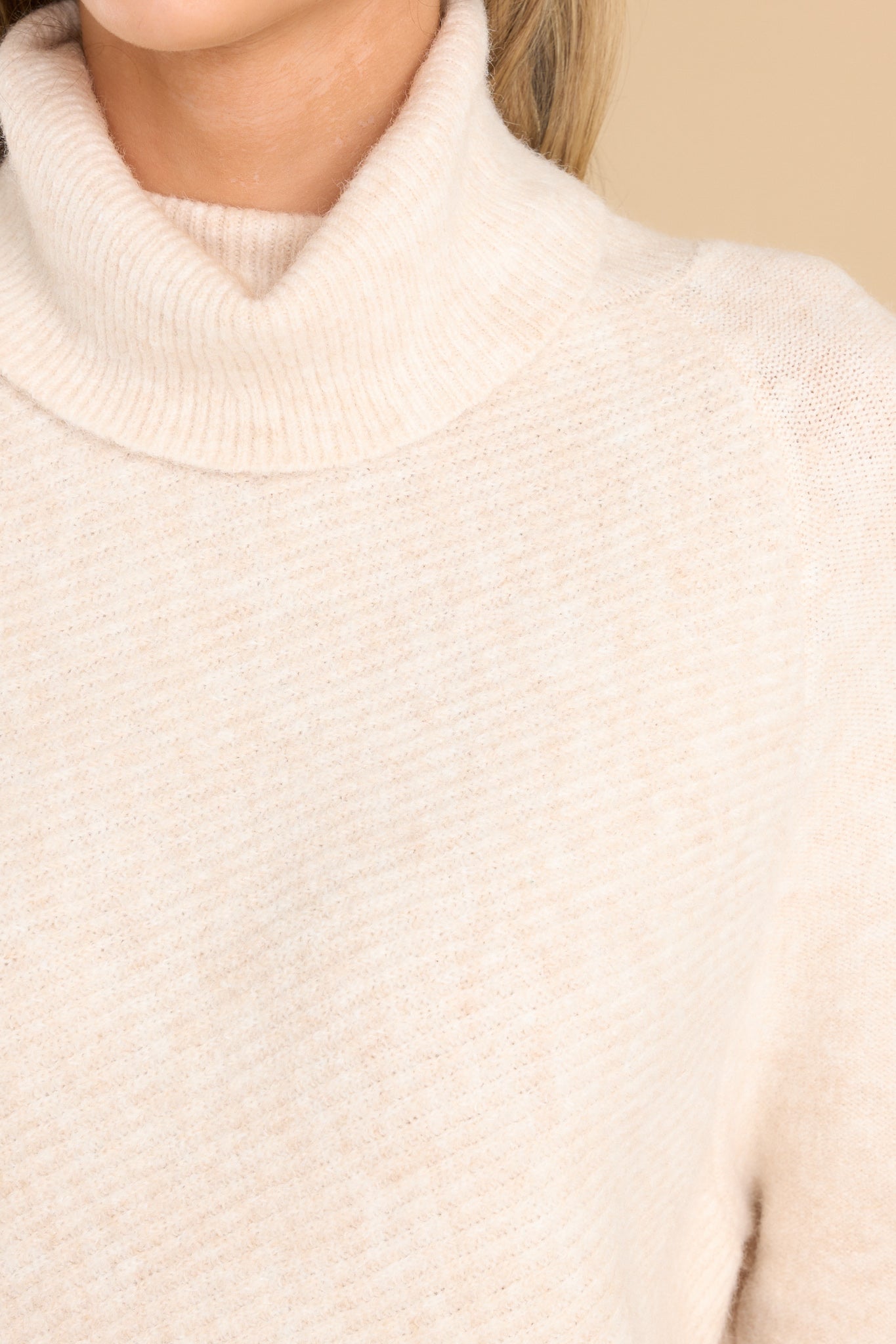 Close up view of this sweater that features a cowl turtle neckline, long sleeves with ribbed cuffs, and a bottom hem that tapers in around the hips.