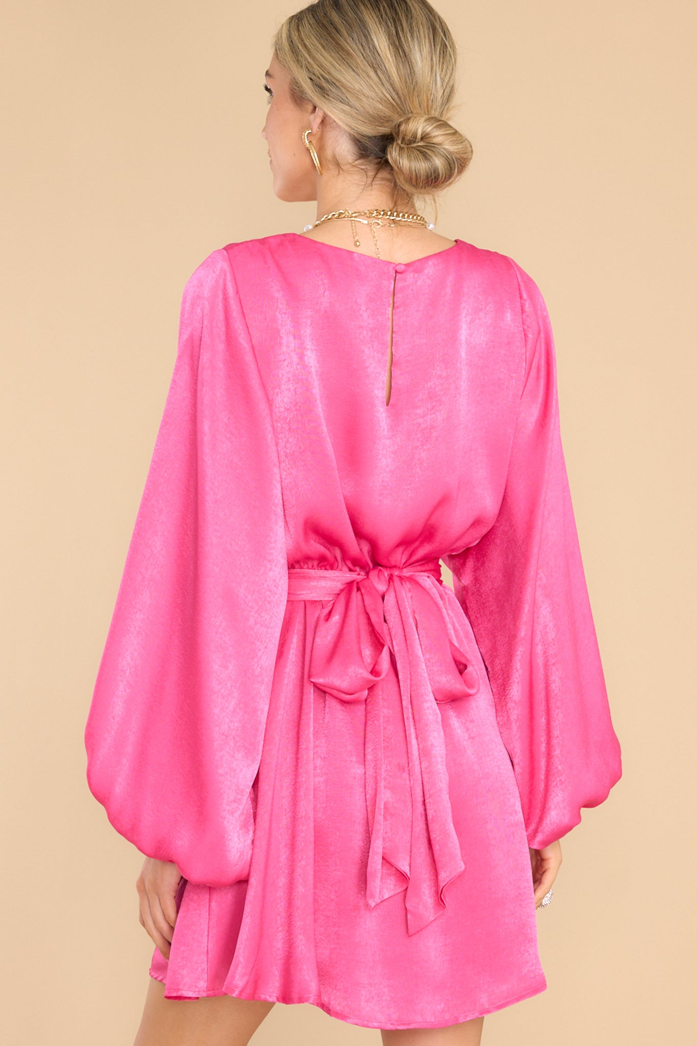 Back view of this dress that features a round neckline, a keyhole with a button closure on the back, flowy sleeves with smocked cuffs, an elastic waistband, a self-tie, and a flowy skirt.