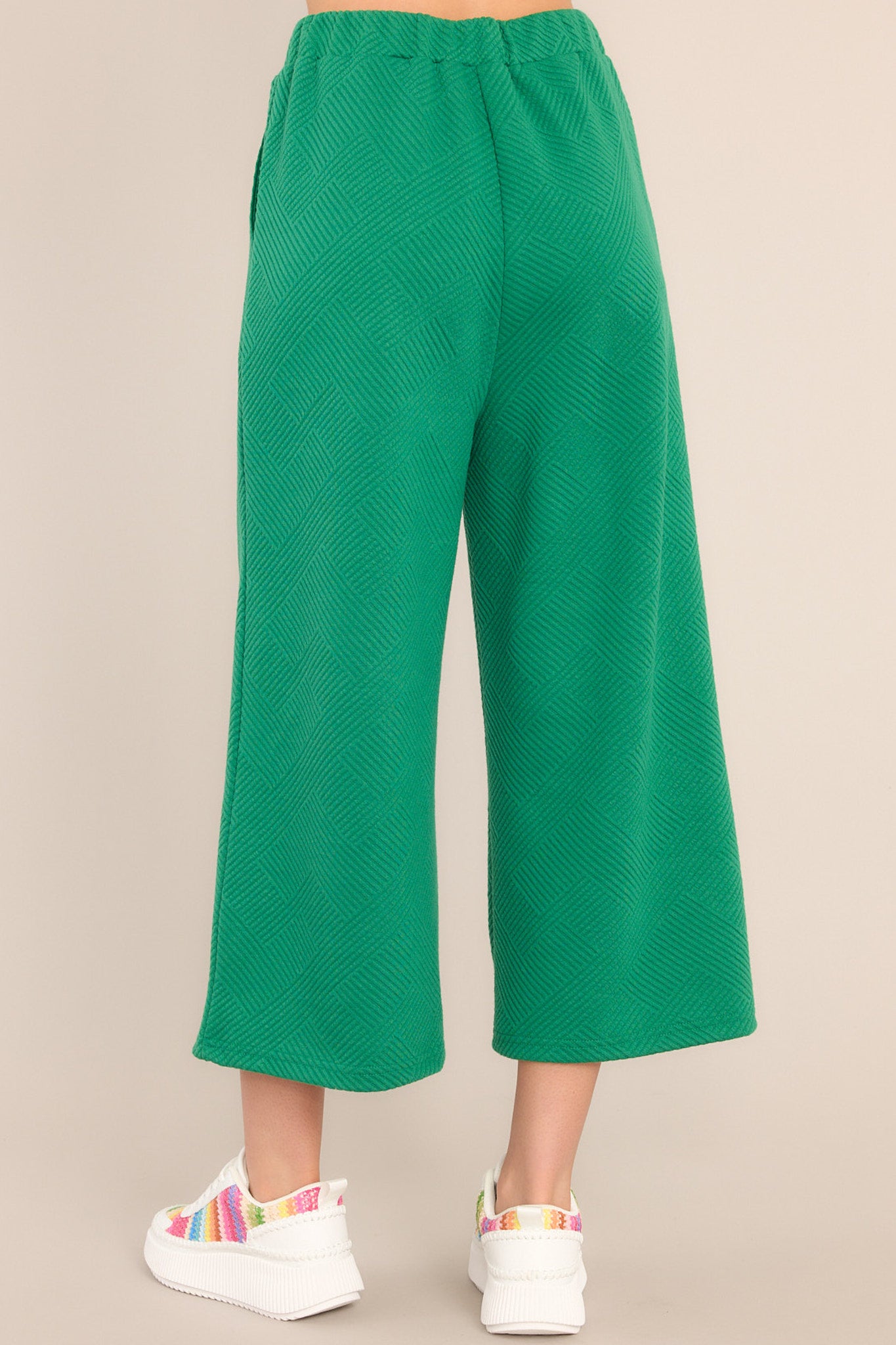 Back view of  these pants that feature a high waisted design, an elastic waistband, functional hip pockets, a textured crisscross design, and a wide leg.