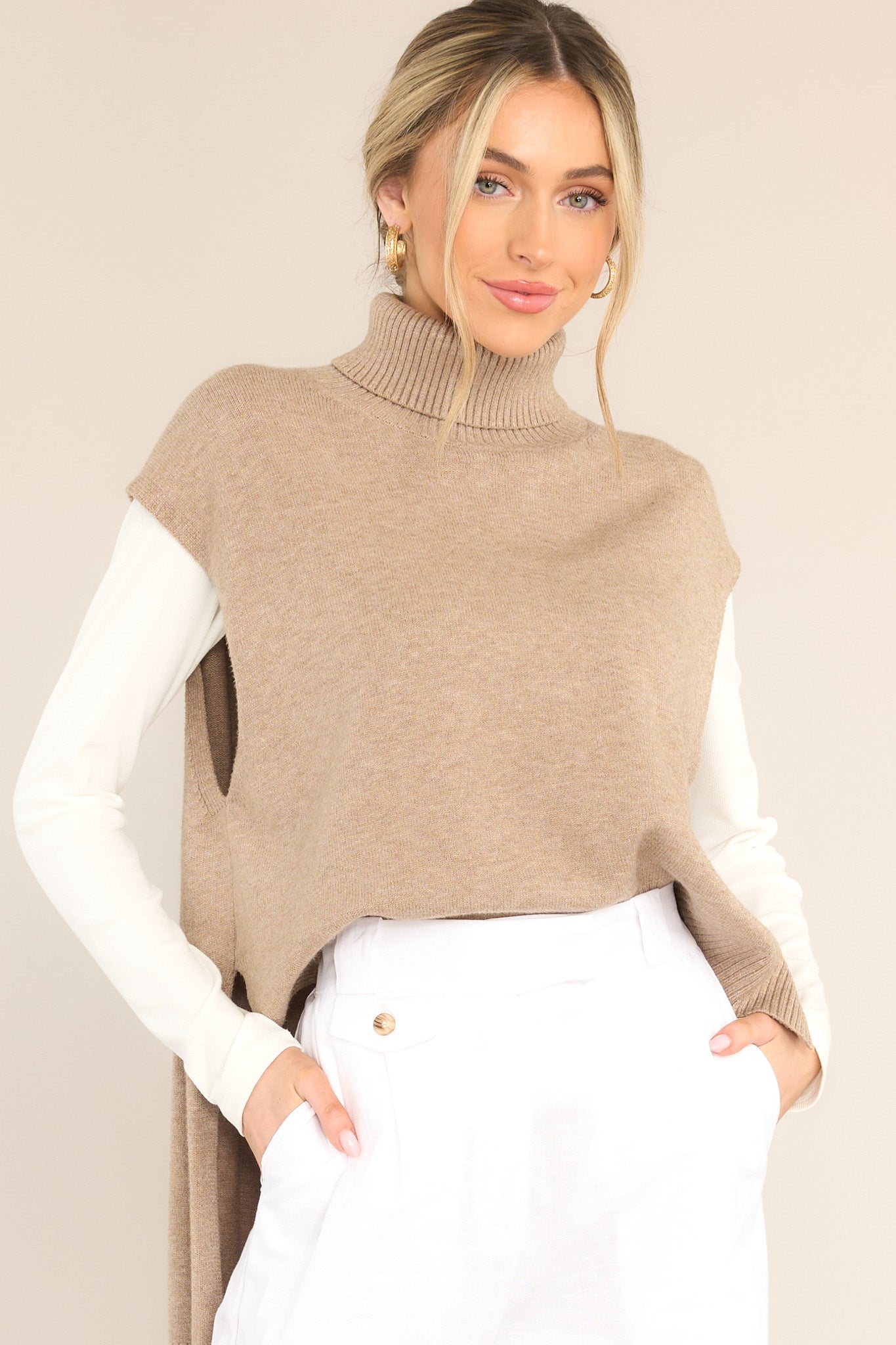 This beige turtleneck sweater vest features a relaxed-fit, turtleneck, rib-knit fabric throughout, slits at sides of hem and longer at back. 