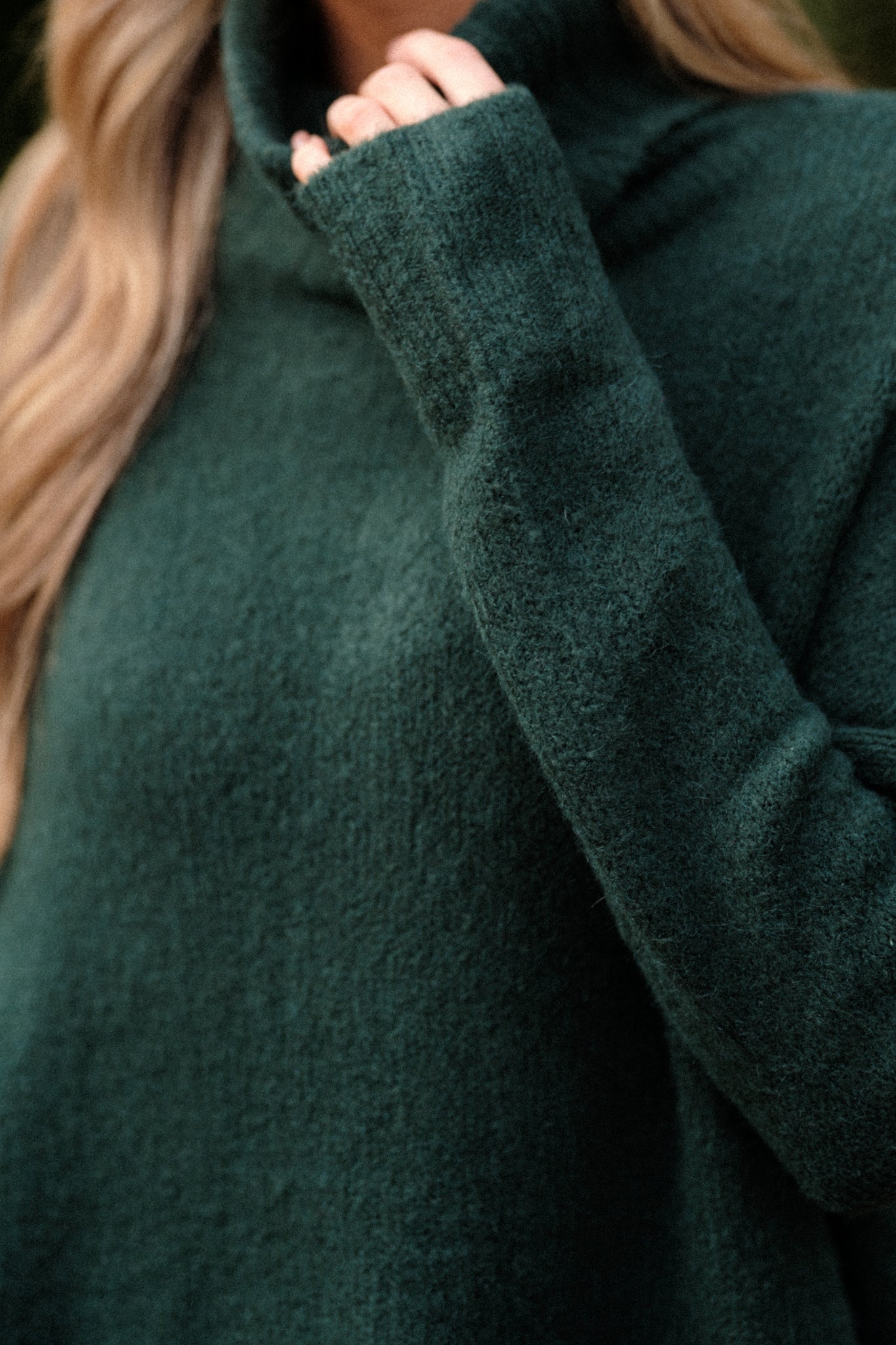 Close up view of this sweater that features a very light eyelash knit design, a turtle cowl neckline, extremely dropped shoulders, and a slight high low hemline.